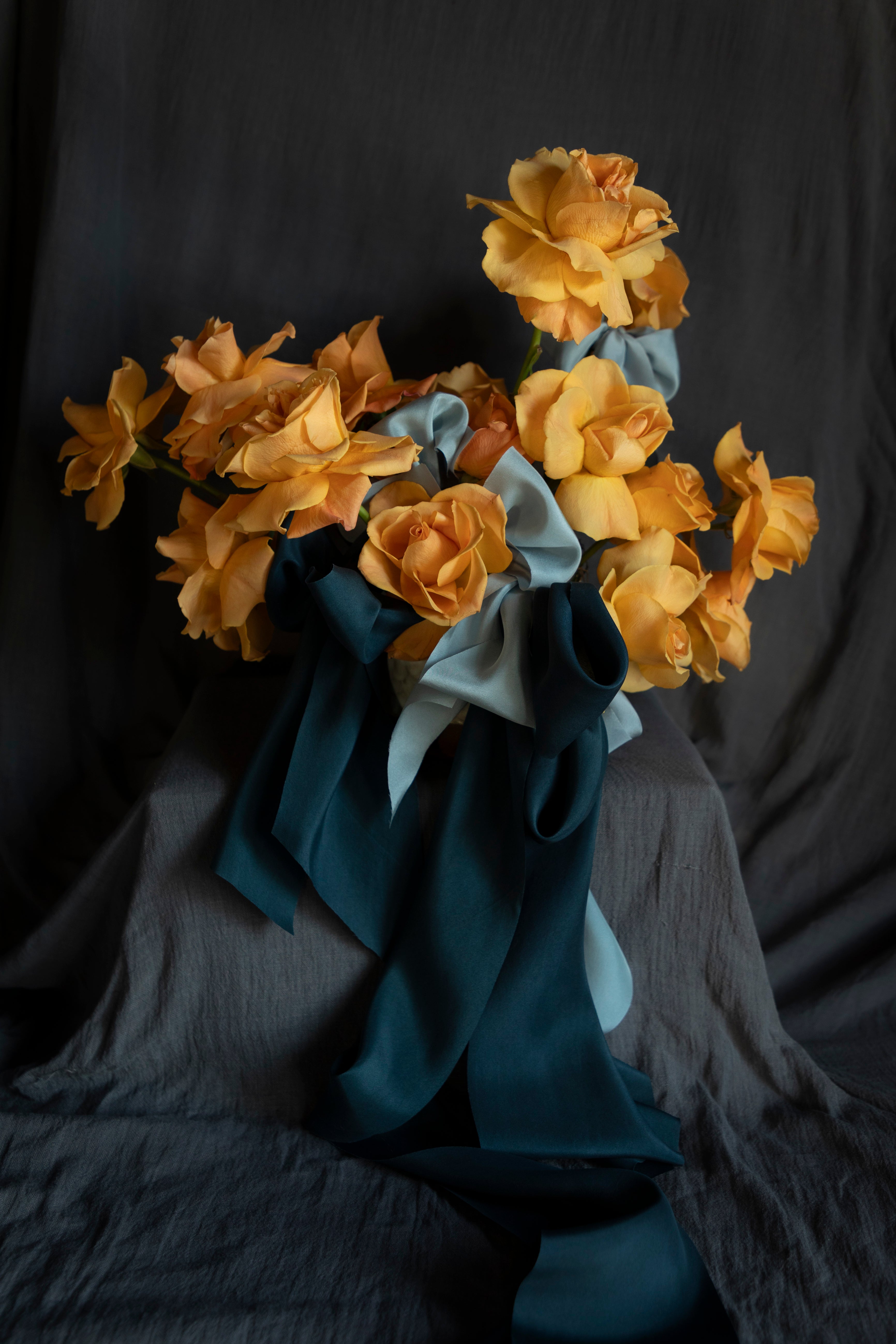 Bouquet of coral rose flowers wrapped with blue silk ribbon bows against a dark background