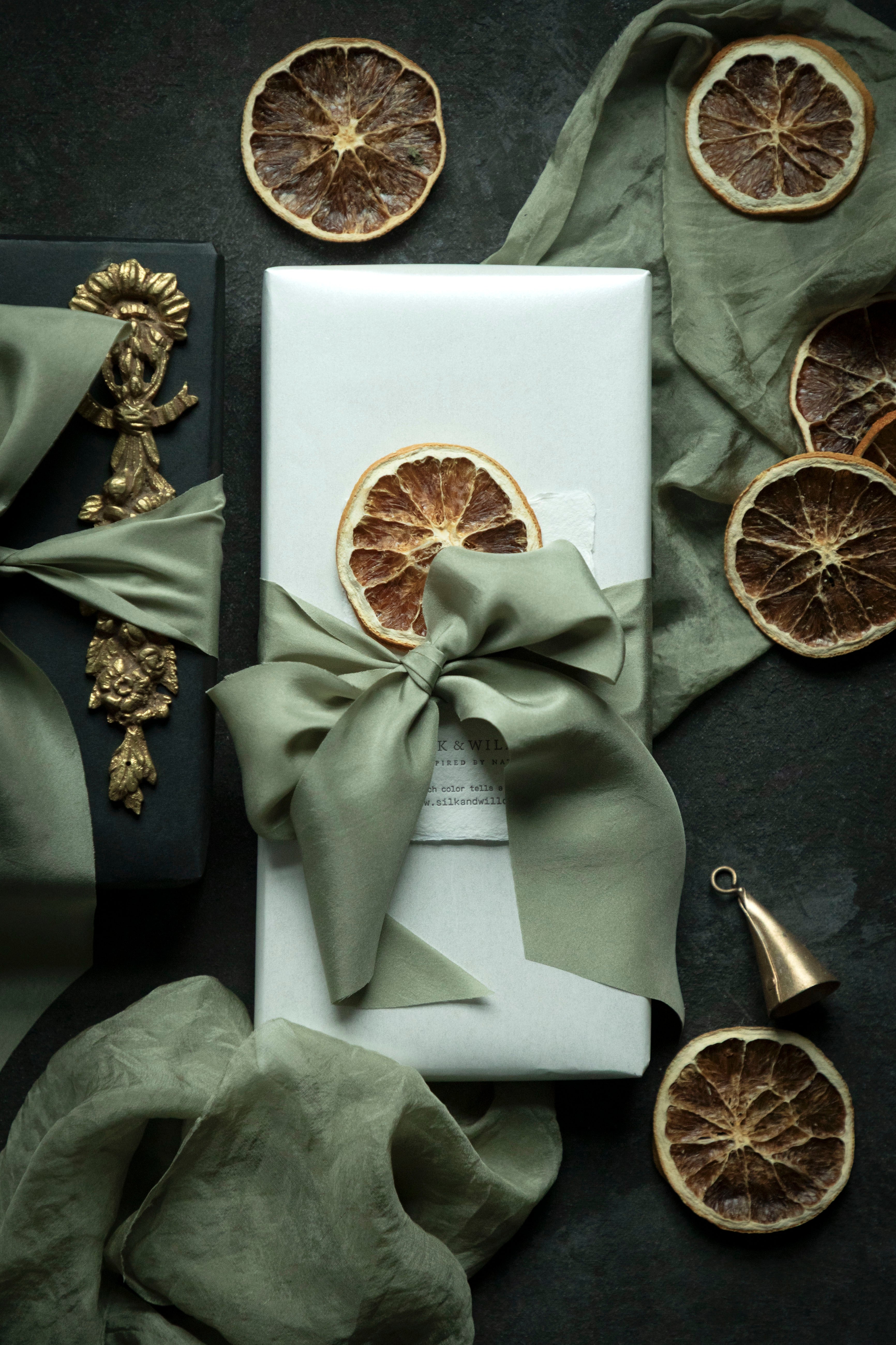 Gift box with a green ribbon and dried oranges on a dark surface