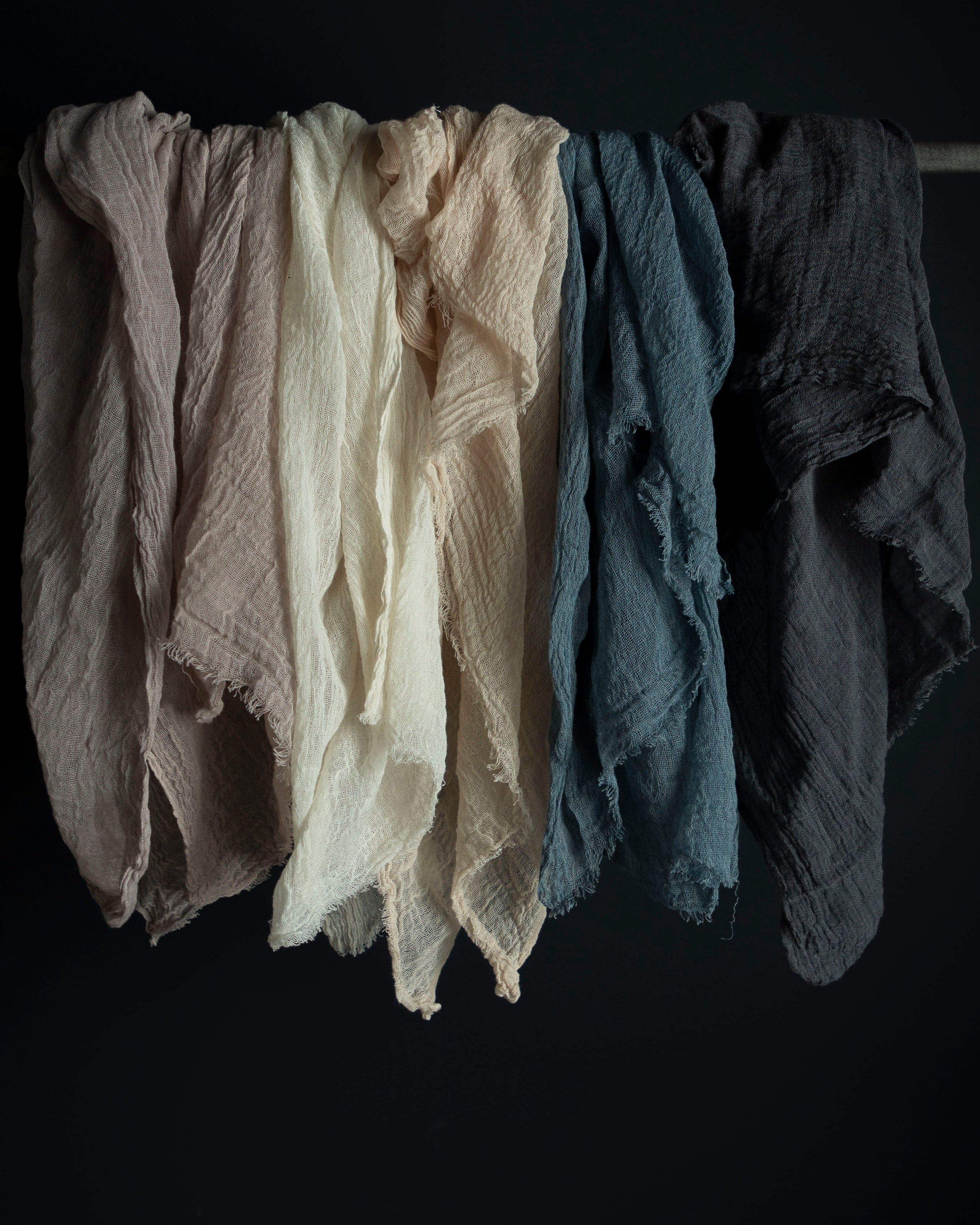 A selection of six handloomed cotton table runners in various colors, hanging against a dark background, showcasing their textures and hues.