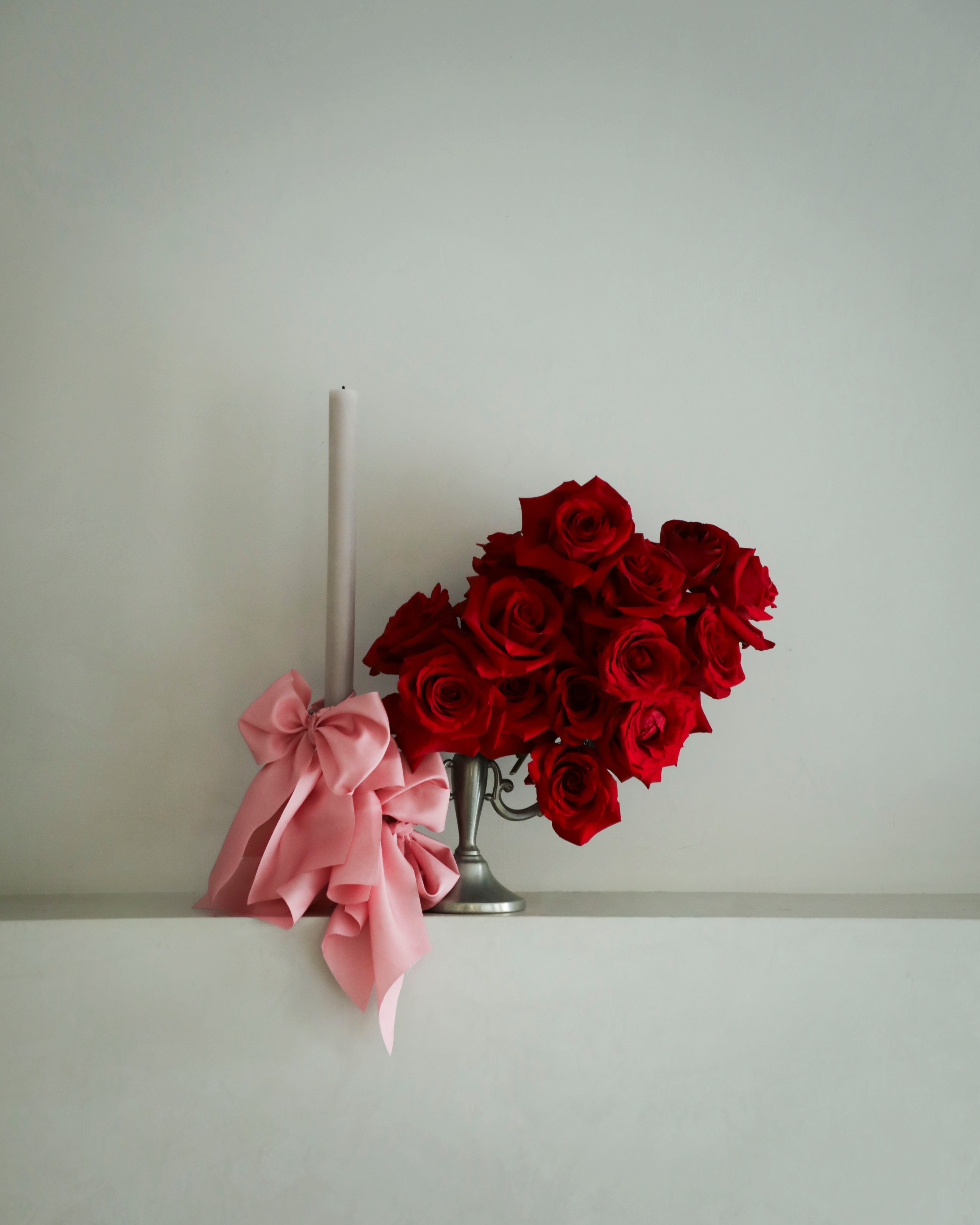 Red roses in a silver vase with a pink bow on a white surface against a light gray background