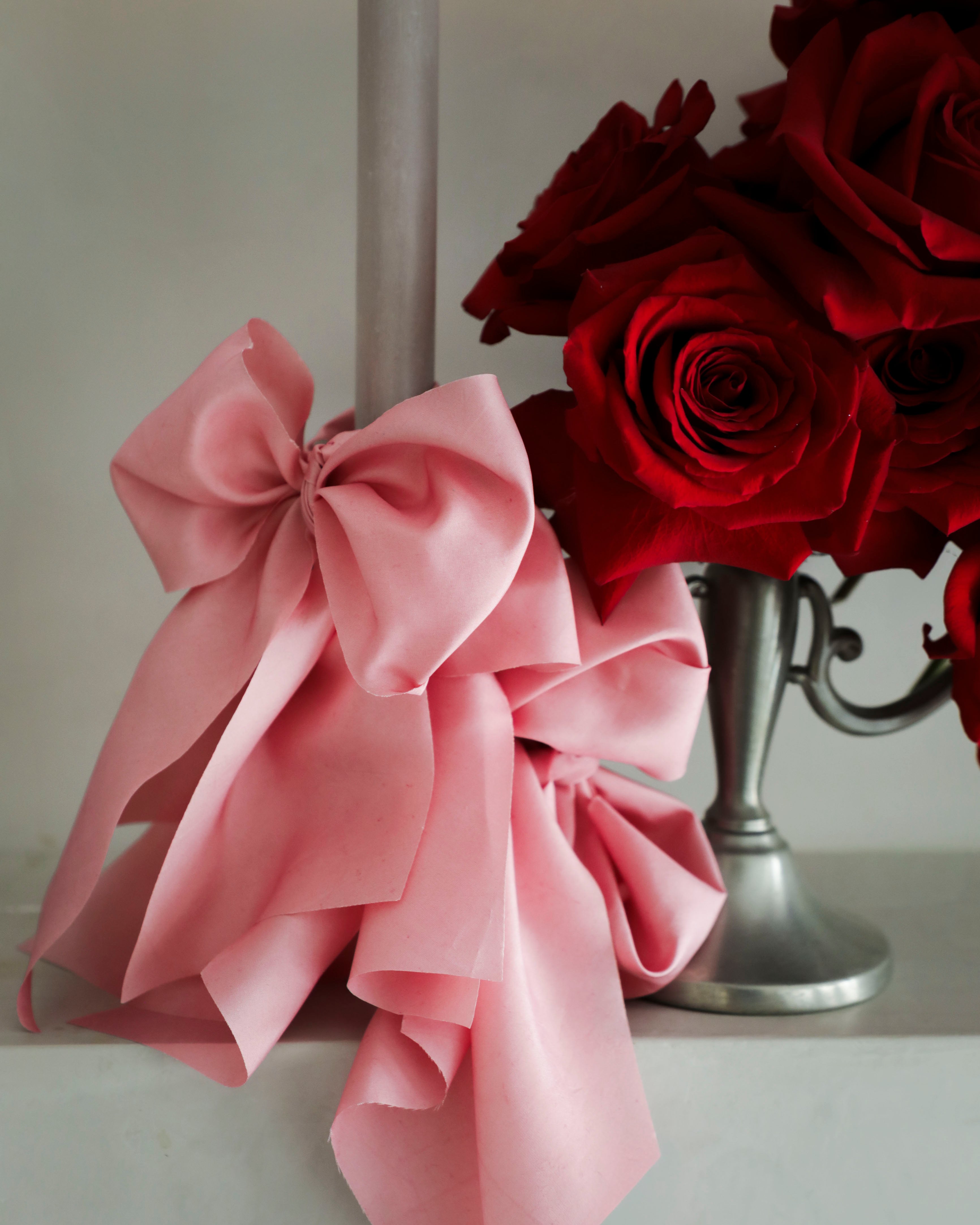 Pink bow and red roses on a white surface with a neutral background