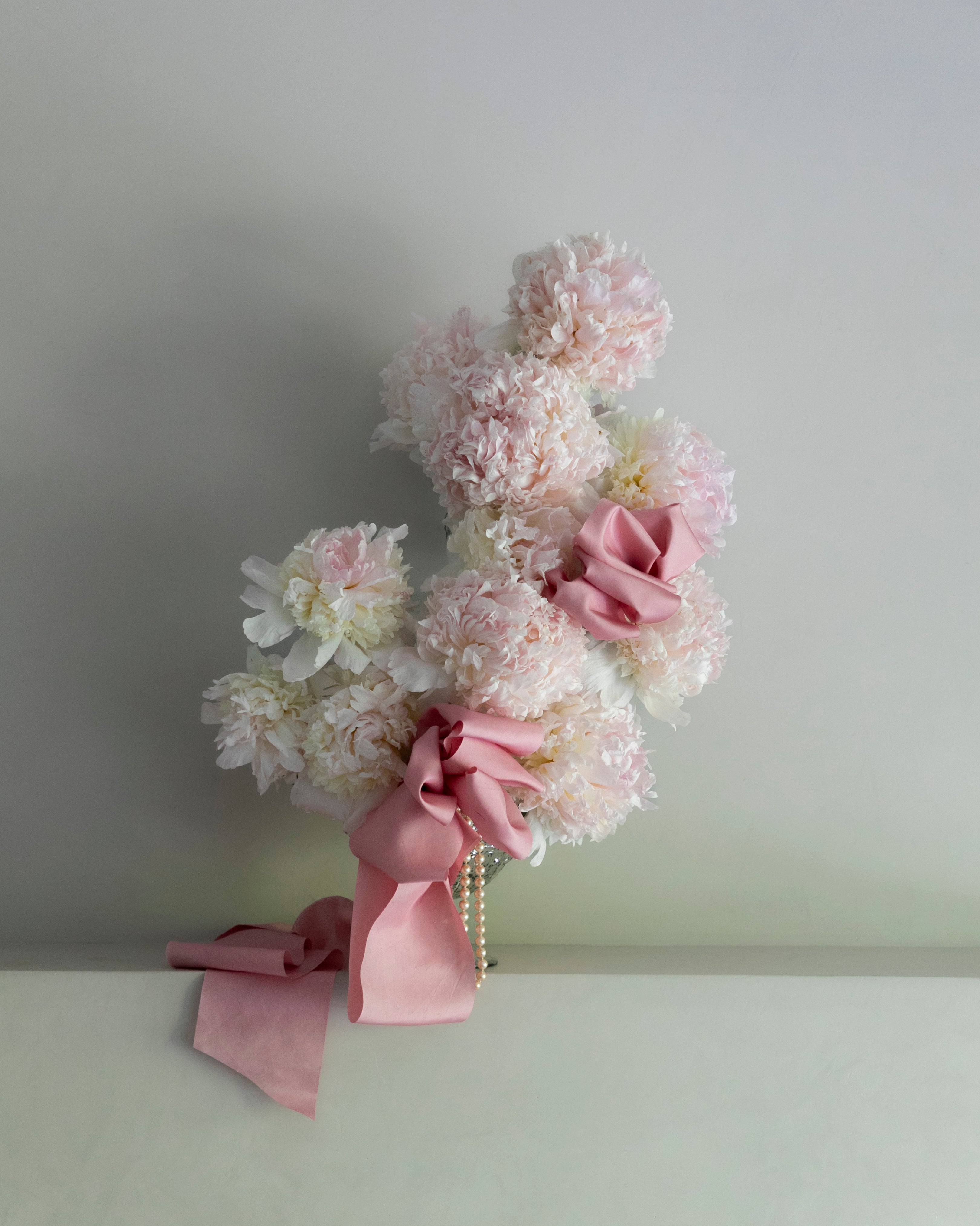 Decorative floral arrangement with peonies and pink ribbons on a plain background