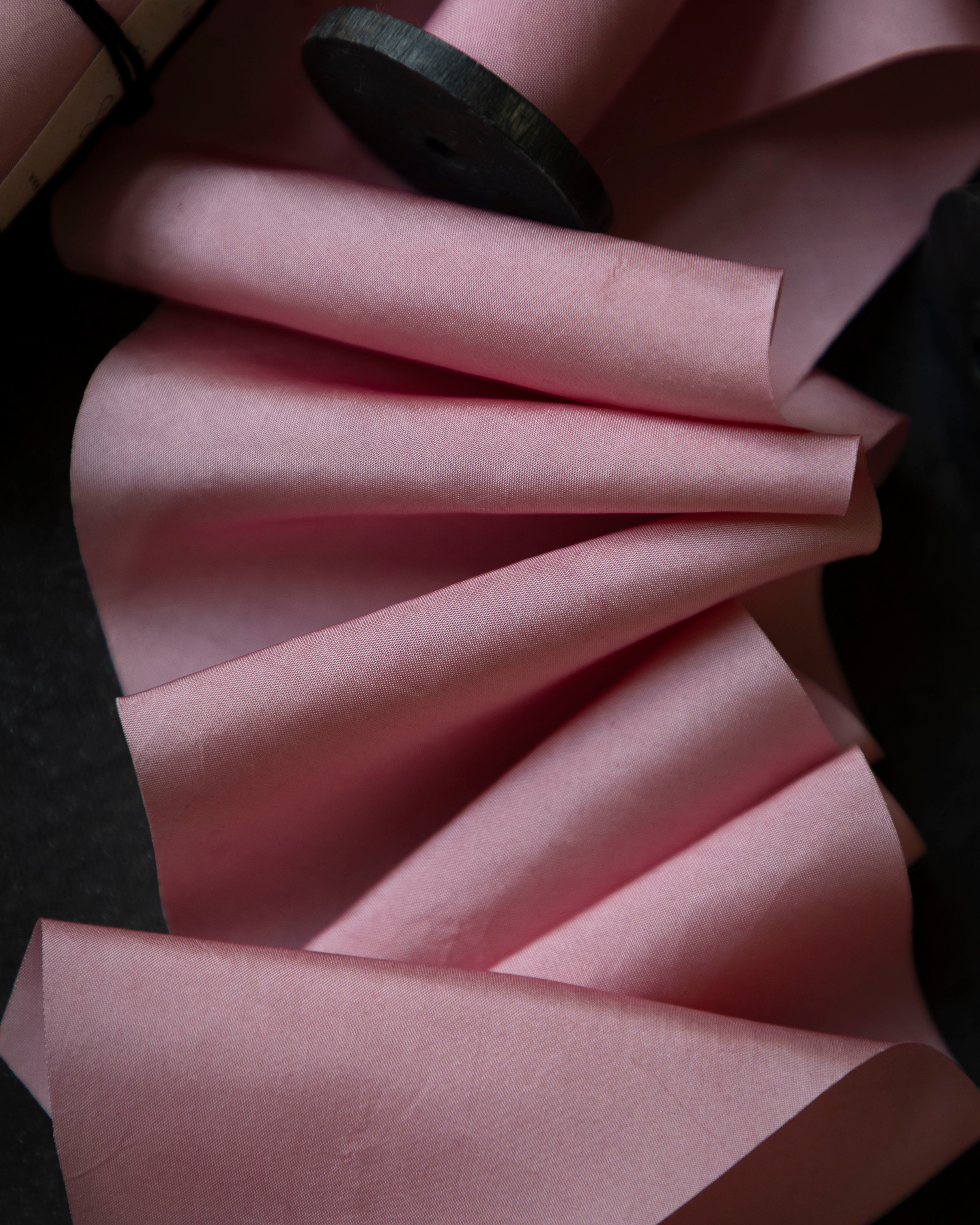 Pink fabric with a wooden spool on a dark background