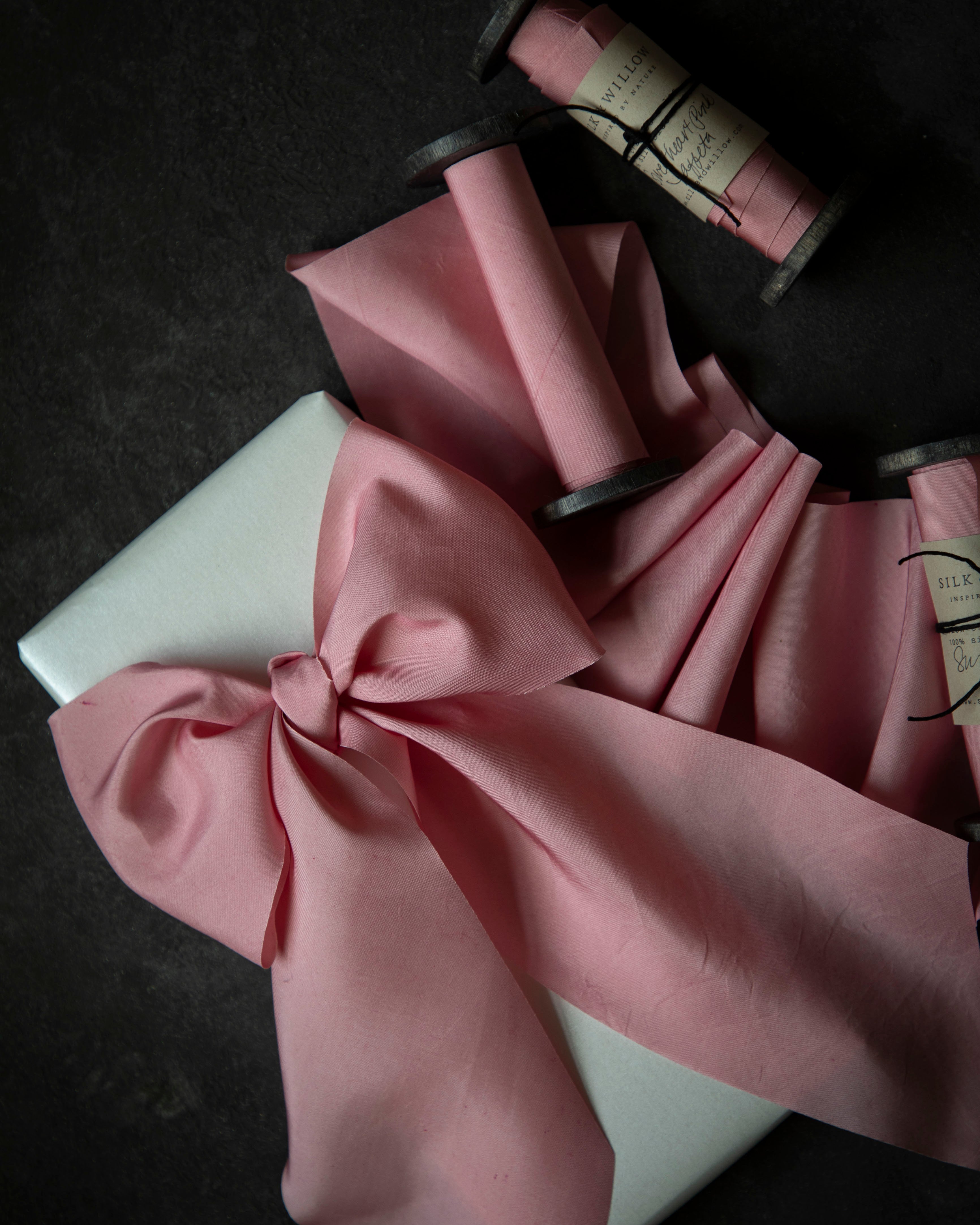 Sweetheart Pink silk ribbon with a bow and spools on a dark surface