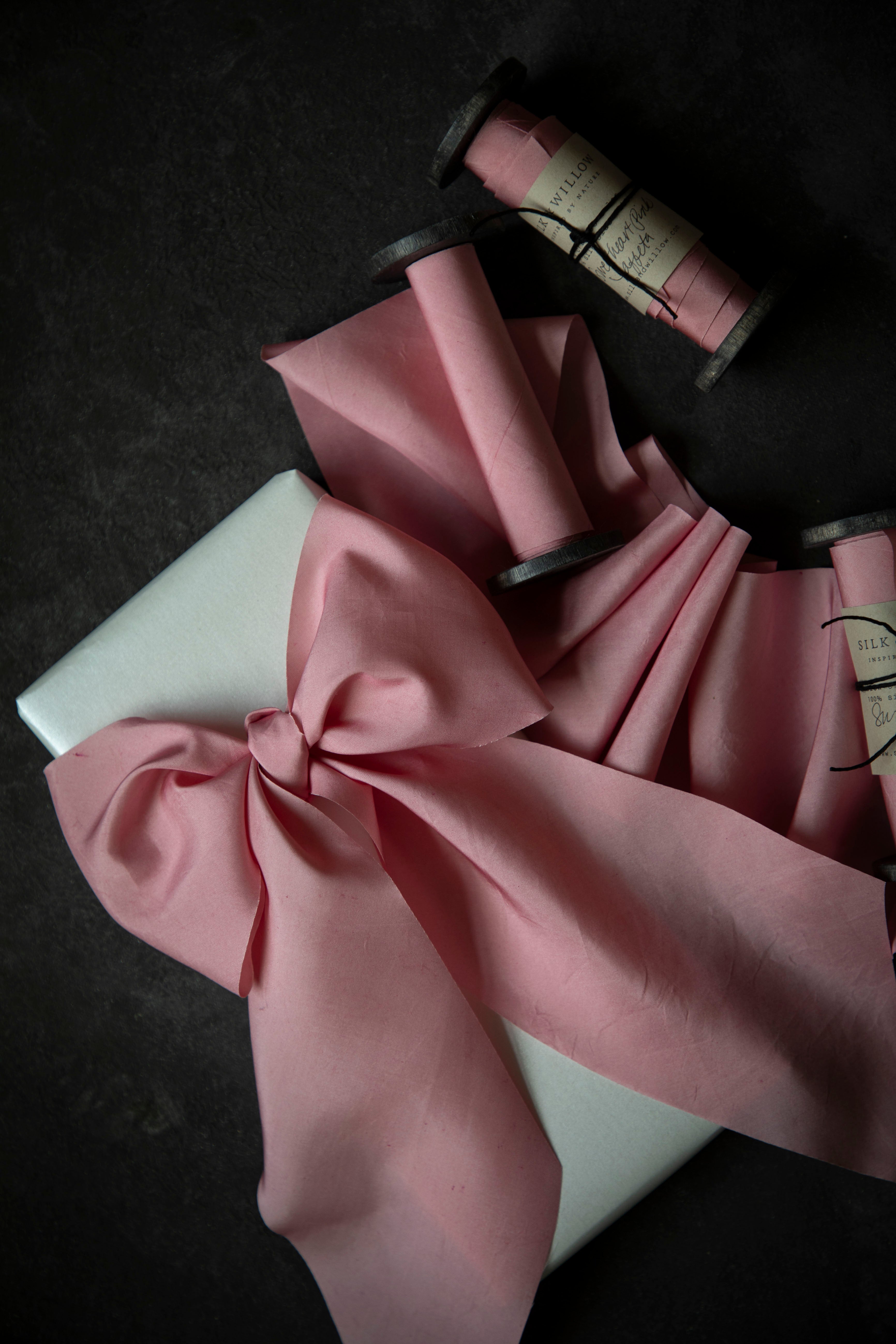 Sweetheart Pink silk ribbon with a bow and spools on a dark surface