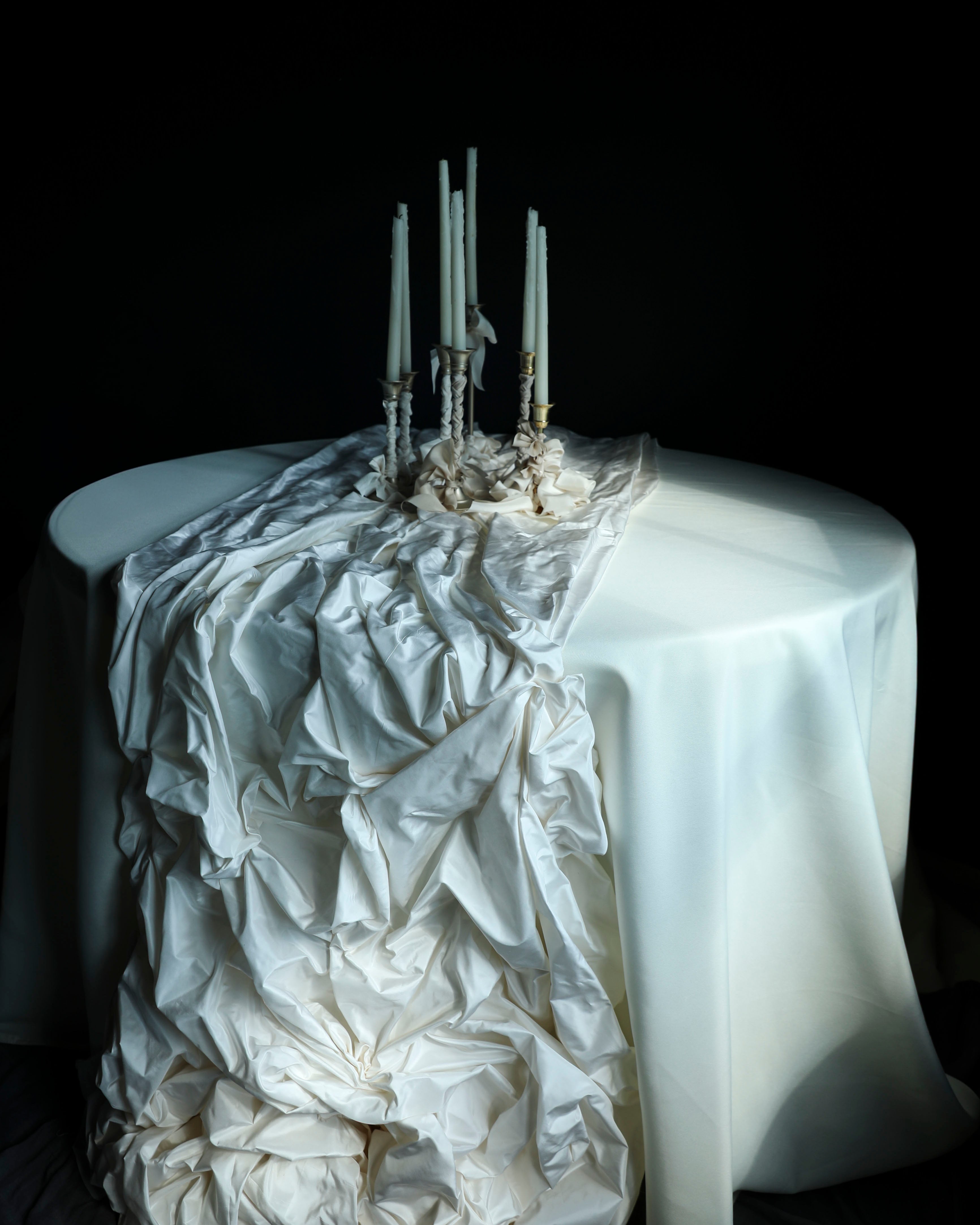 Decorative table with ruffled white tablecloth and candles against a black background