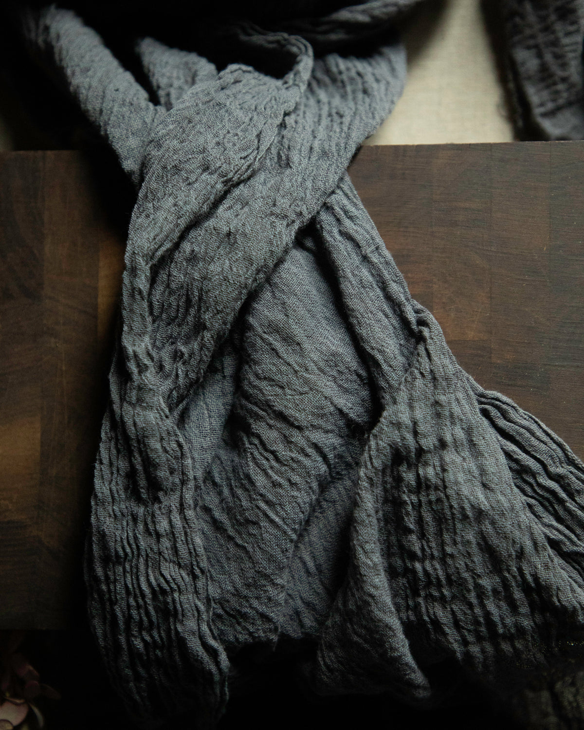 A dark gray crinkled gauze scarf draped over a dark wooden surface.