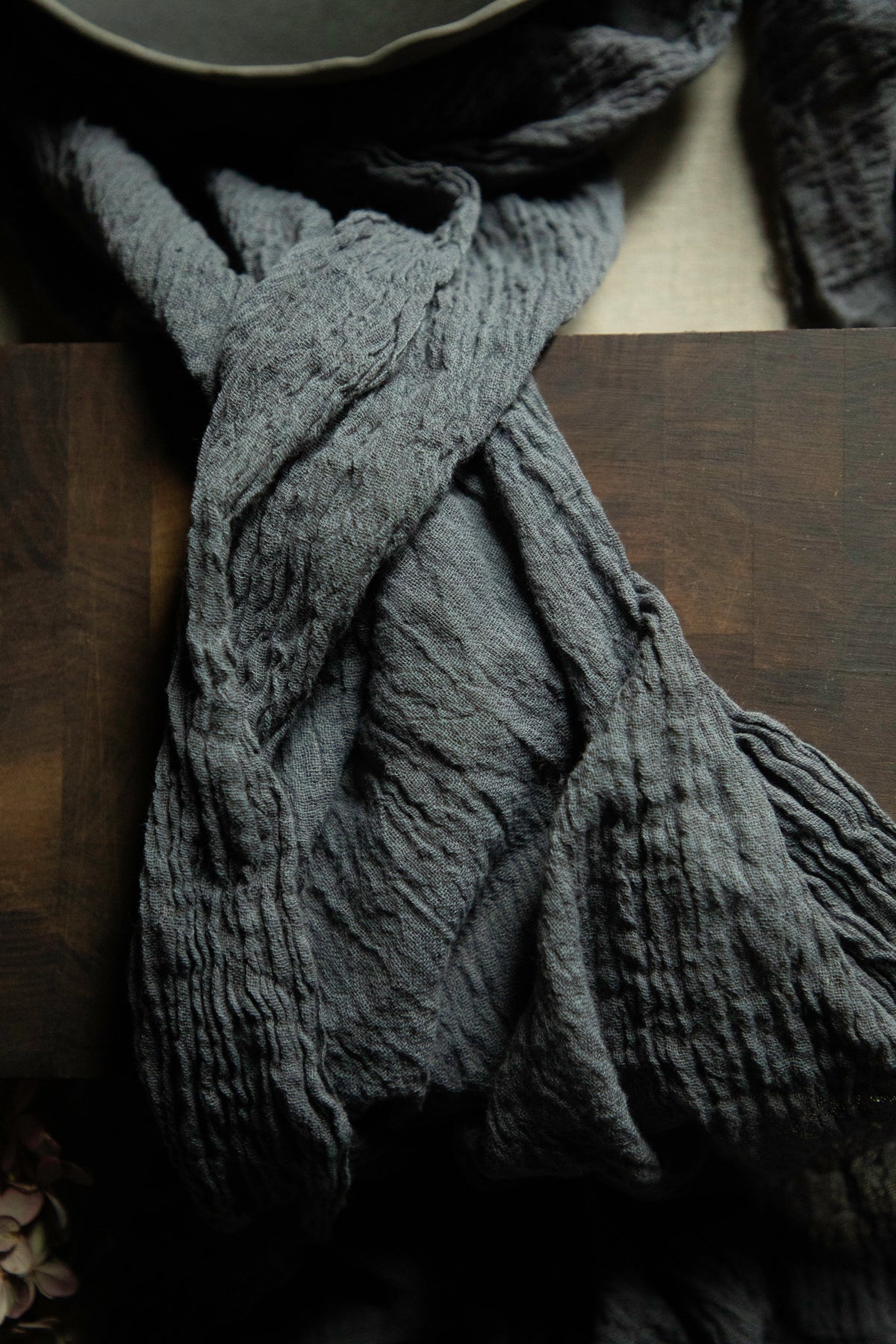 A dark gray crinkled gauze scarf draped over a dark wooden surface.