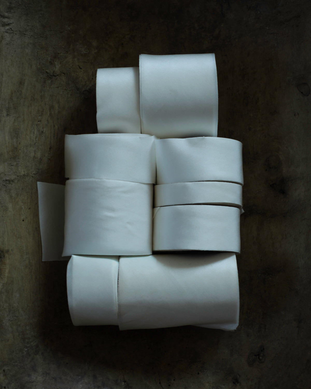 A stack of white fabric ribbon rolls arranged on a dark, textured surface.