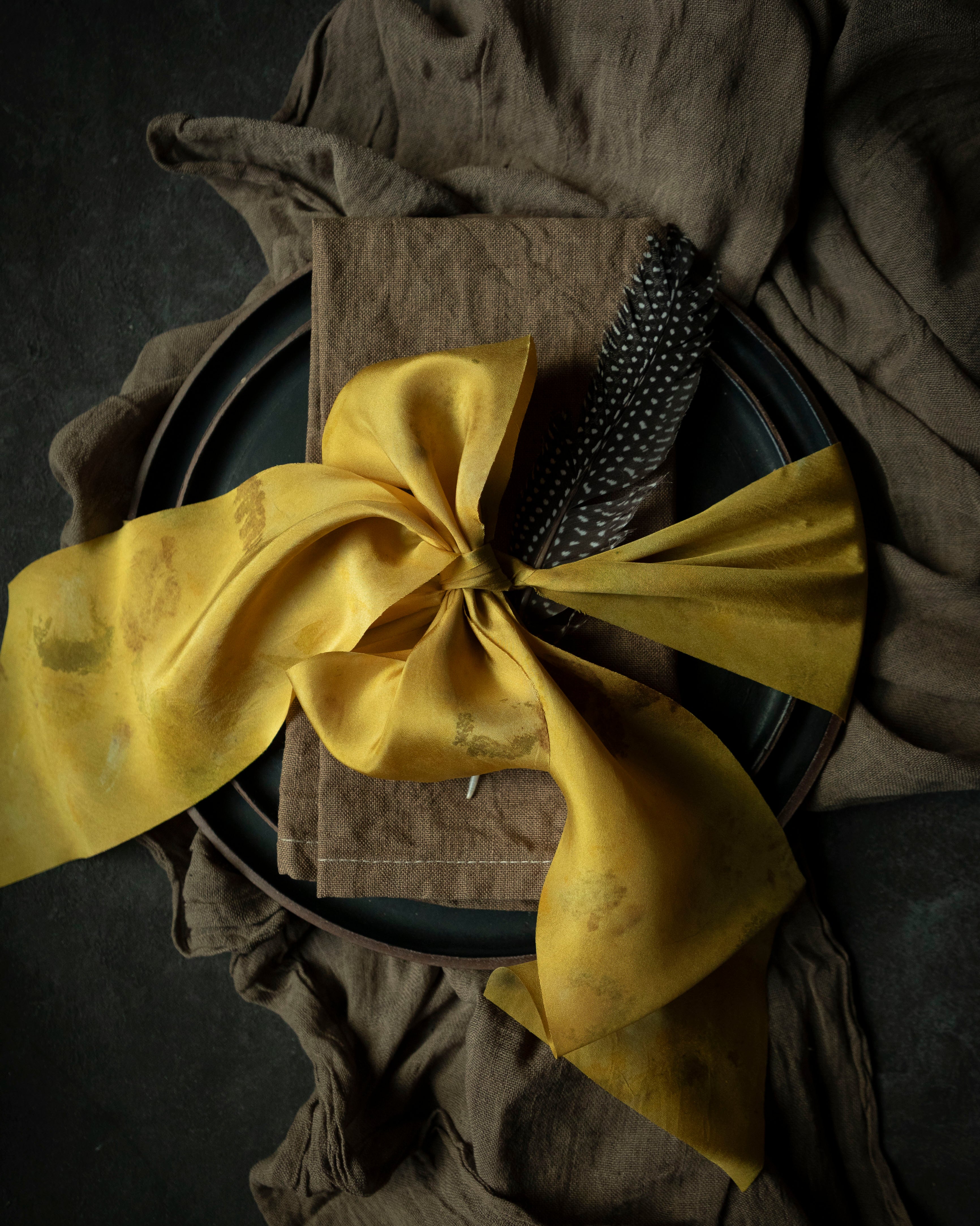 walnut dyed napkin on place setting tied with a yellow ribbon on a black background