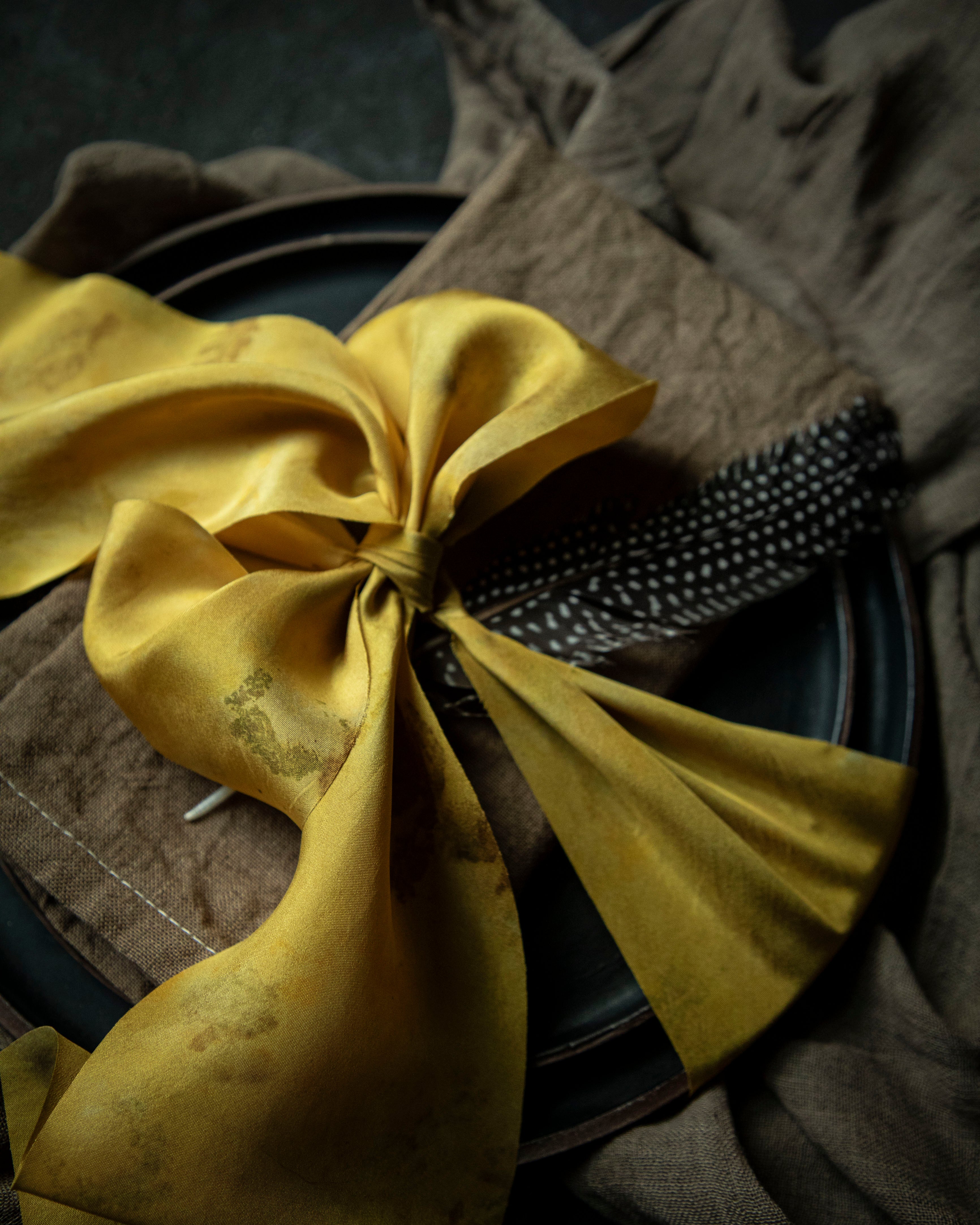 walnut dyed napkin on place setting tied with a yellow ribbon on a black background
