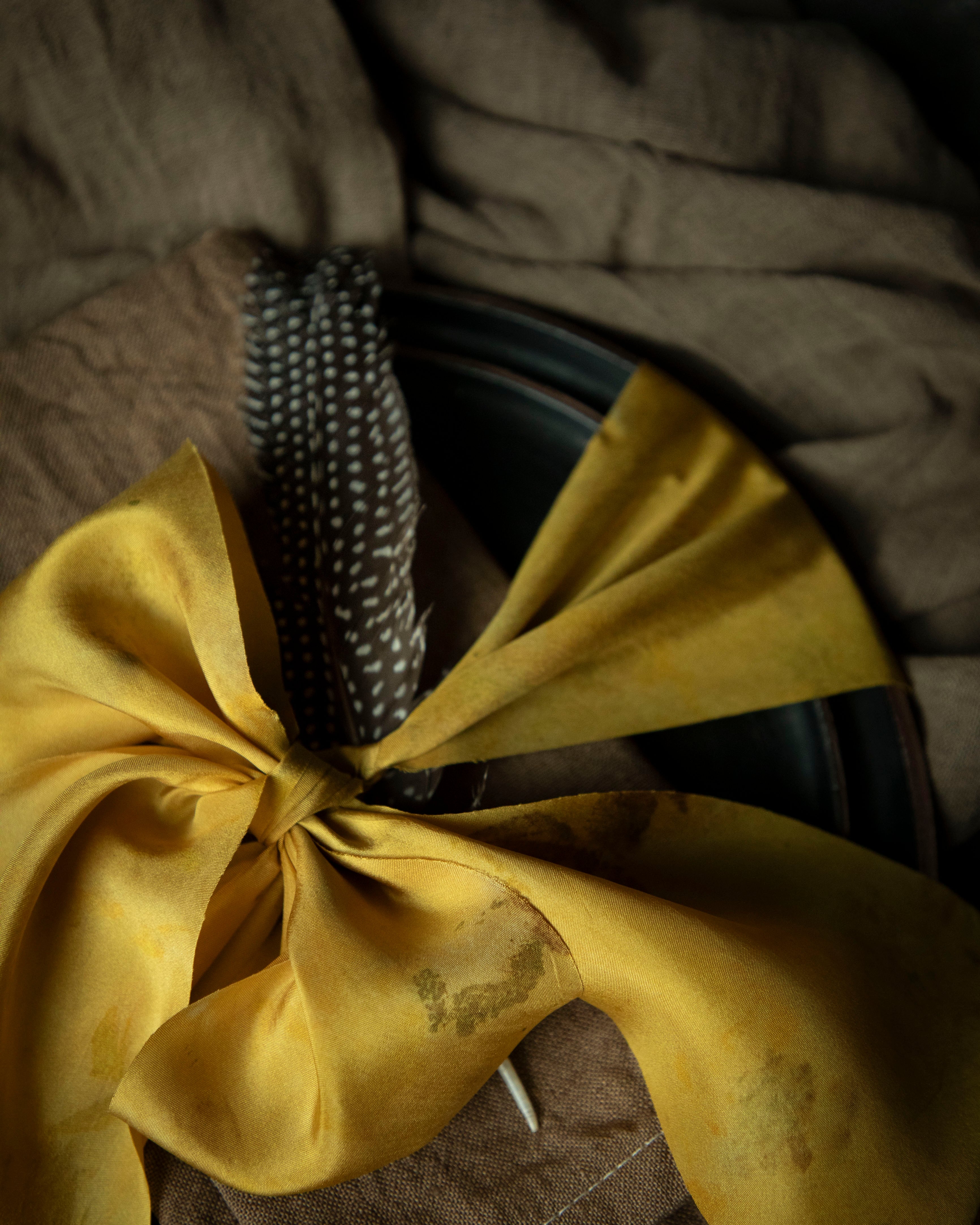 walnut dyed napkin on place setting tied with a yellow ribbon on a black background