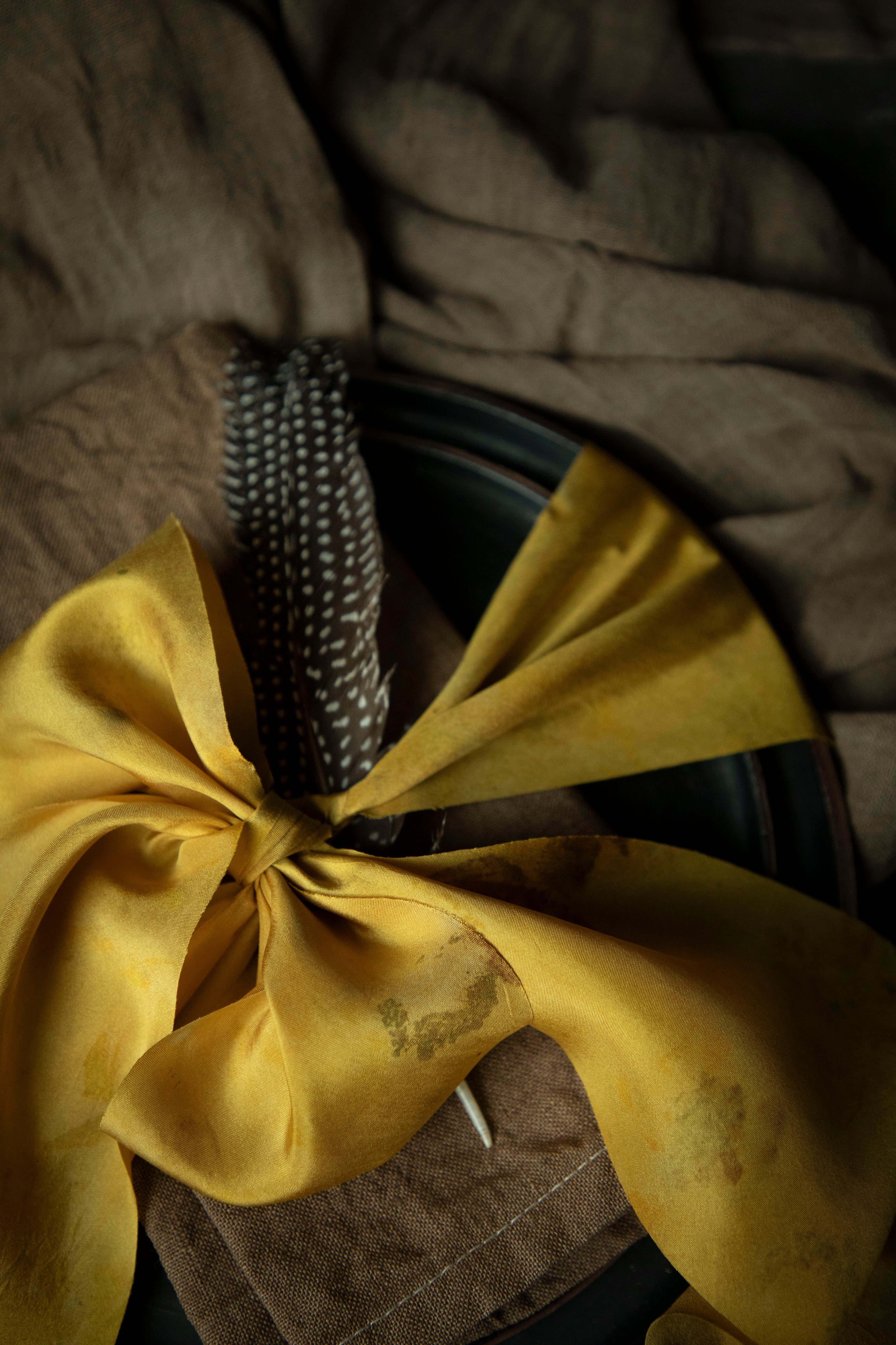 walnut dyed napkin on place setting tied with a yellow ribbon on a black background