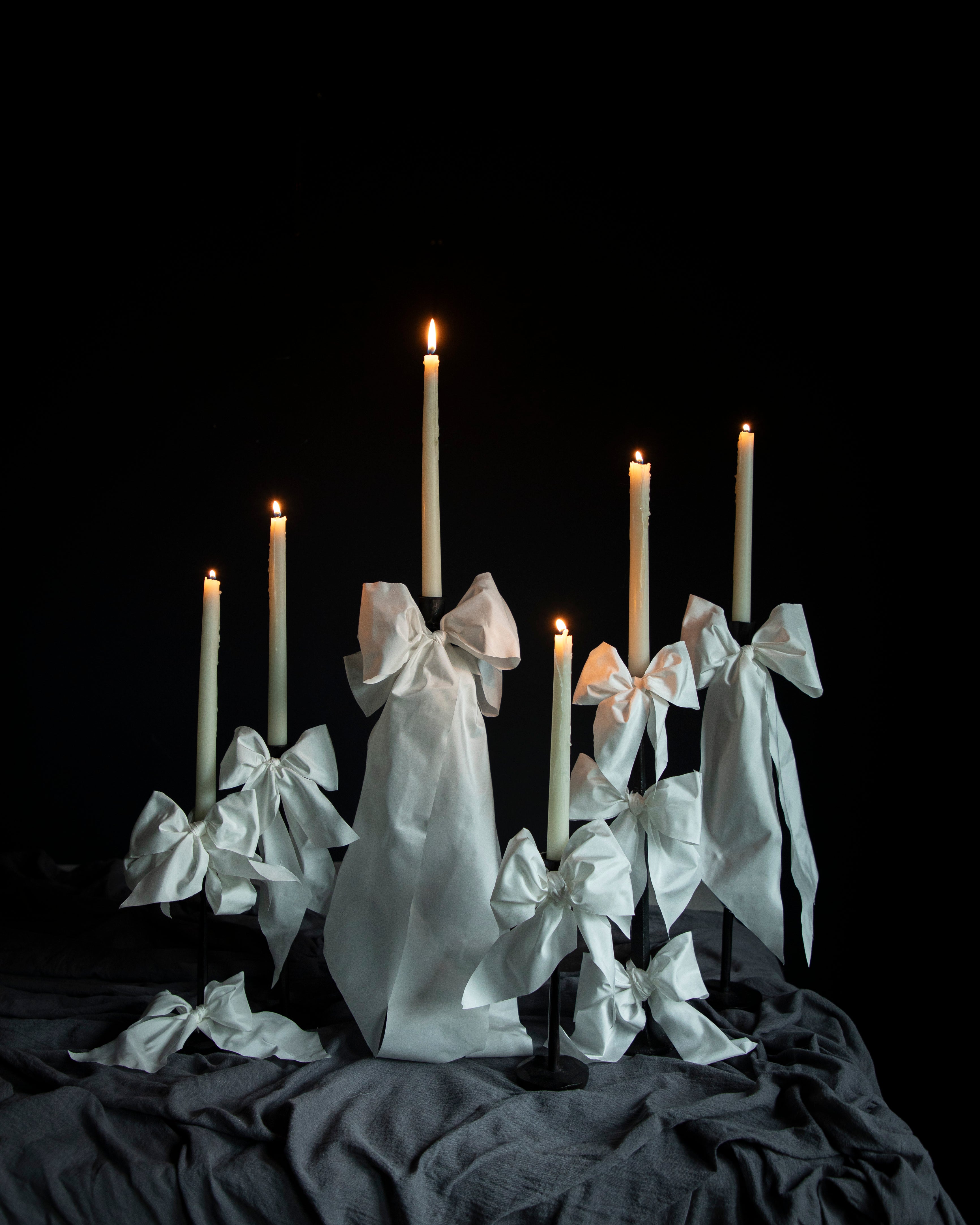Candle holder with white ribbons and lit candles against a black background