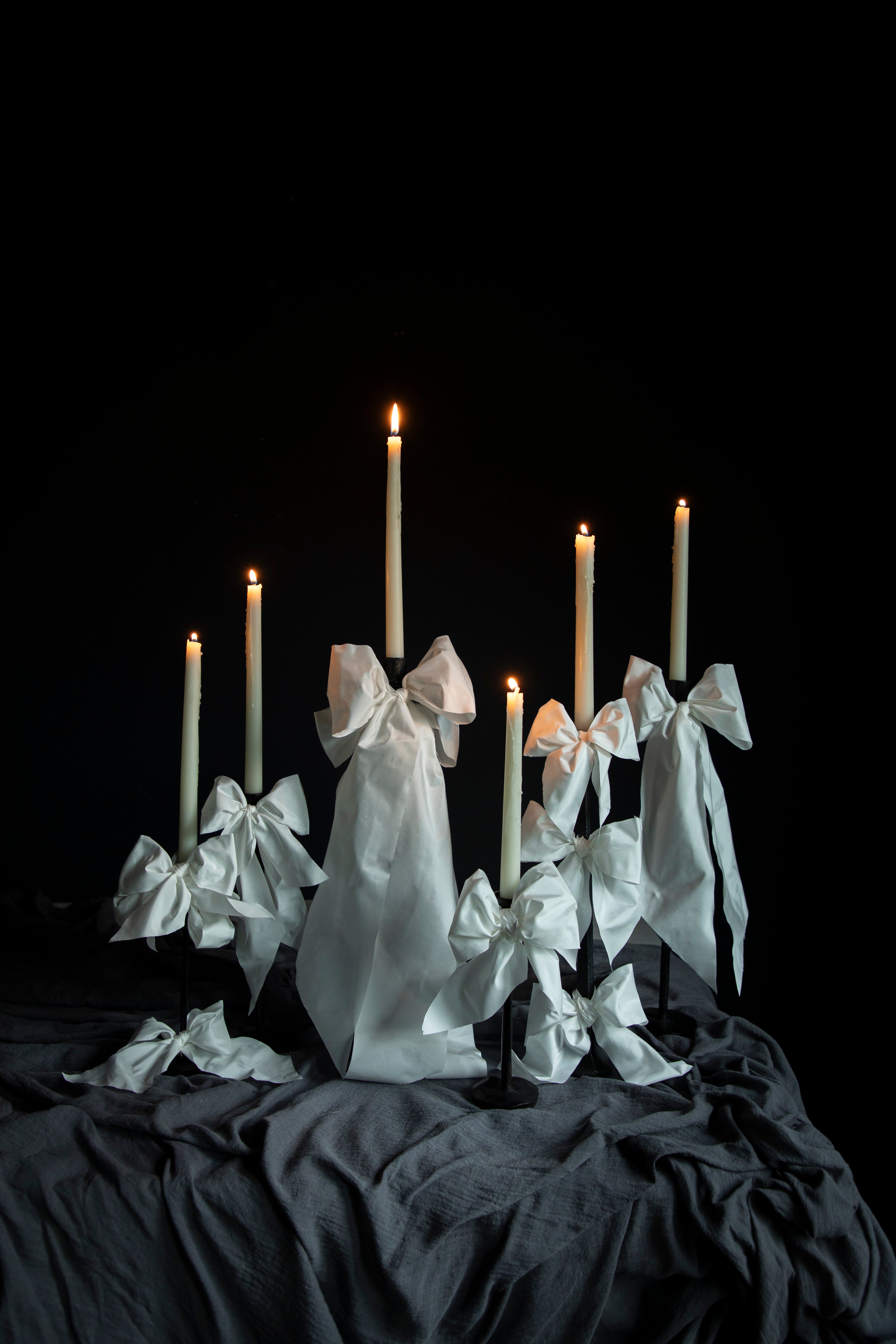 Candle holder with white ribbons and lit candles against a black background