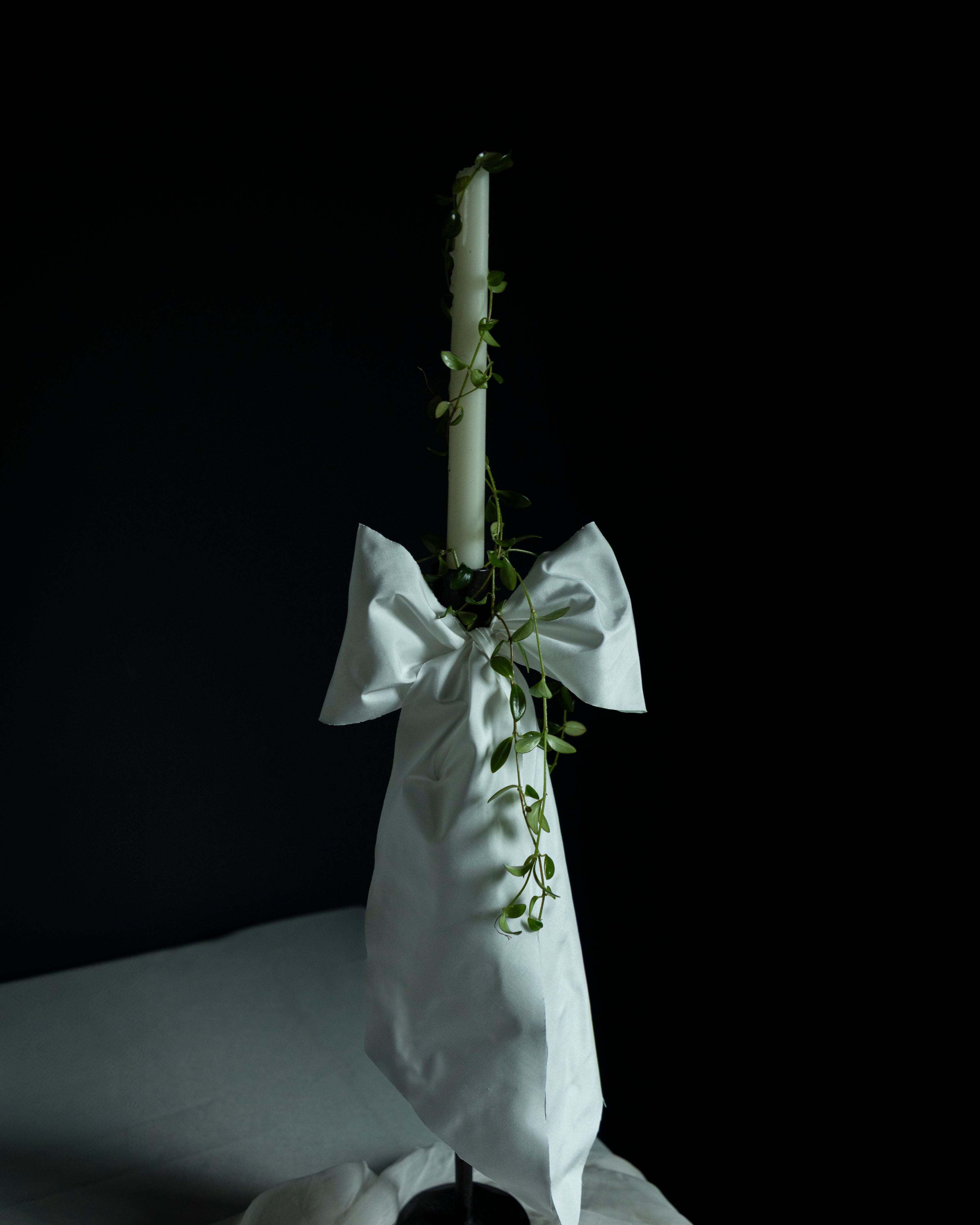 White candle in a holder with a decorative bow on a dark background