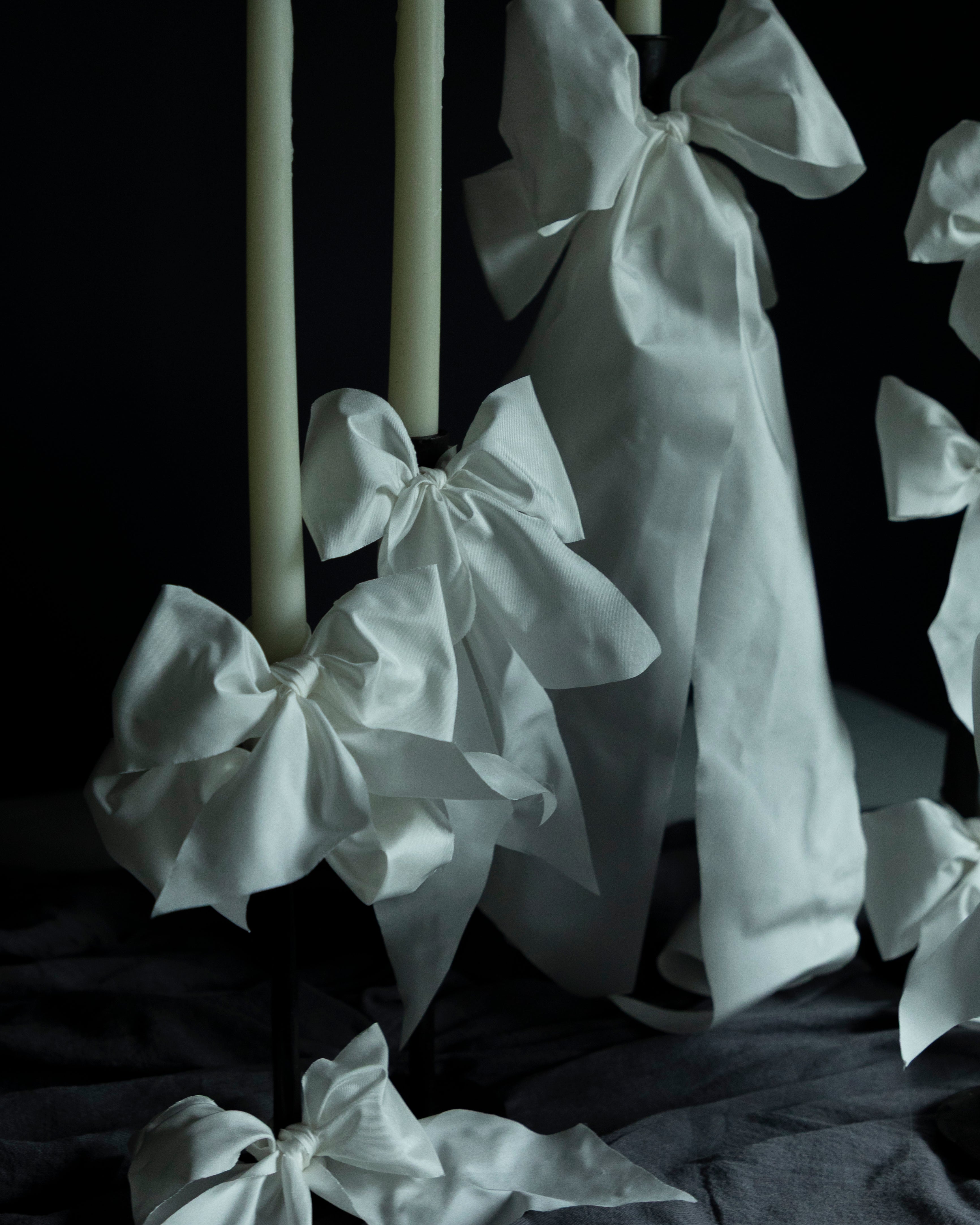 White fabric bows tied around candles on a dark background