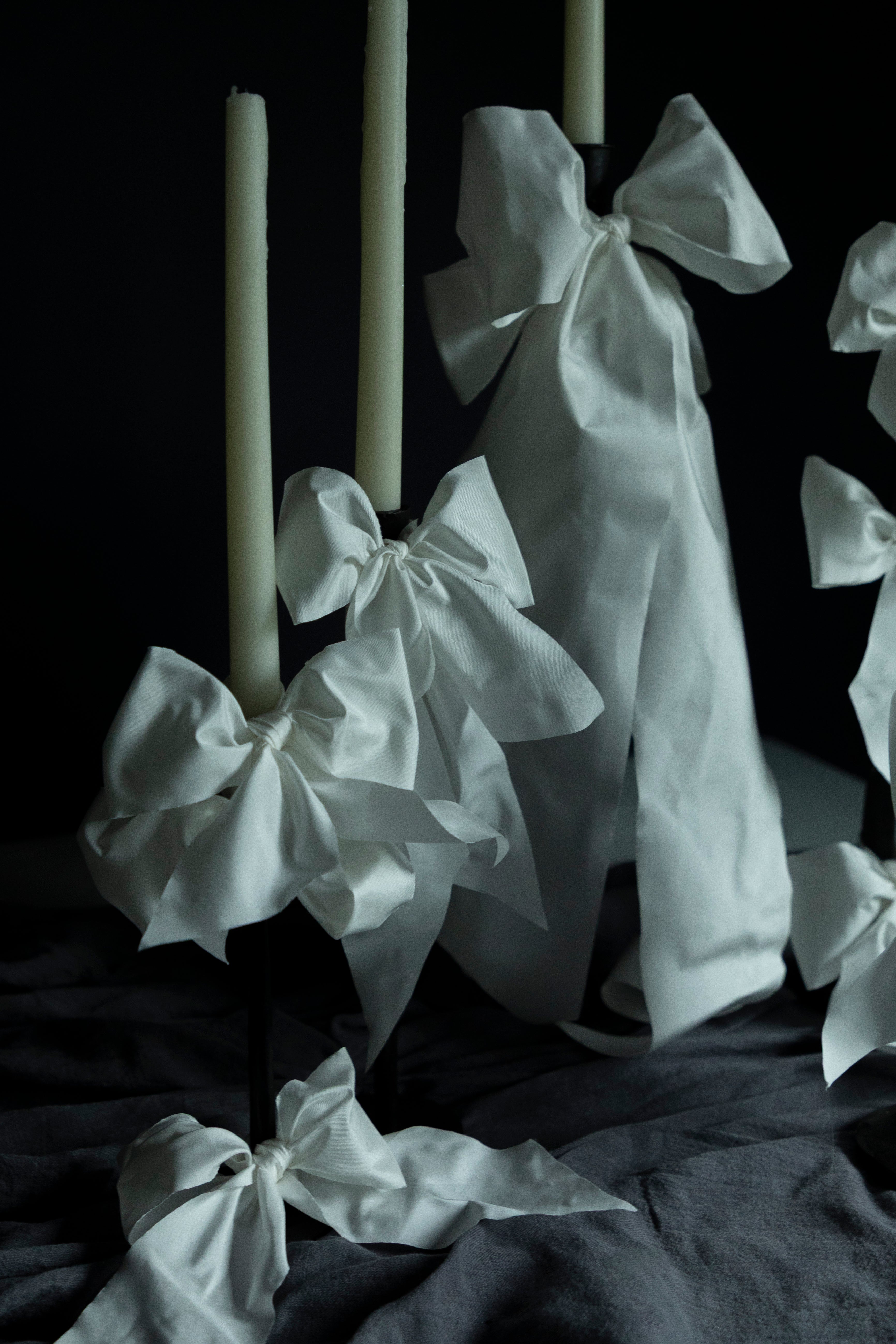 White fabric bows tied around candles on a dark background