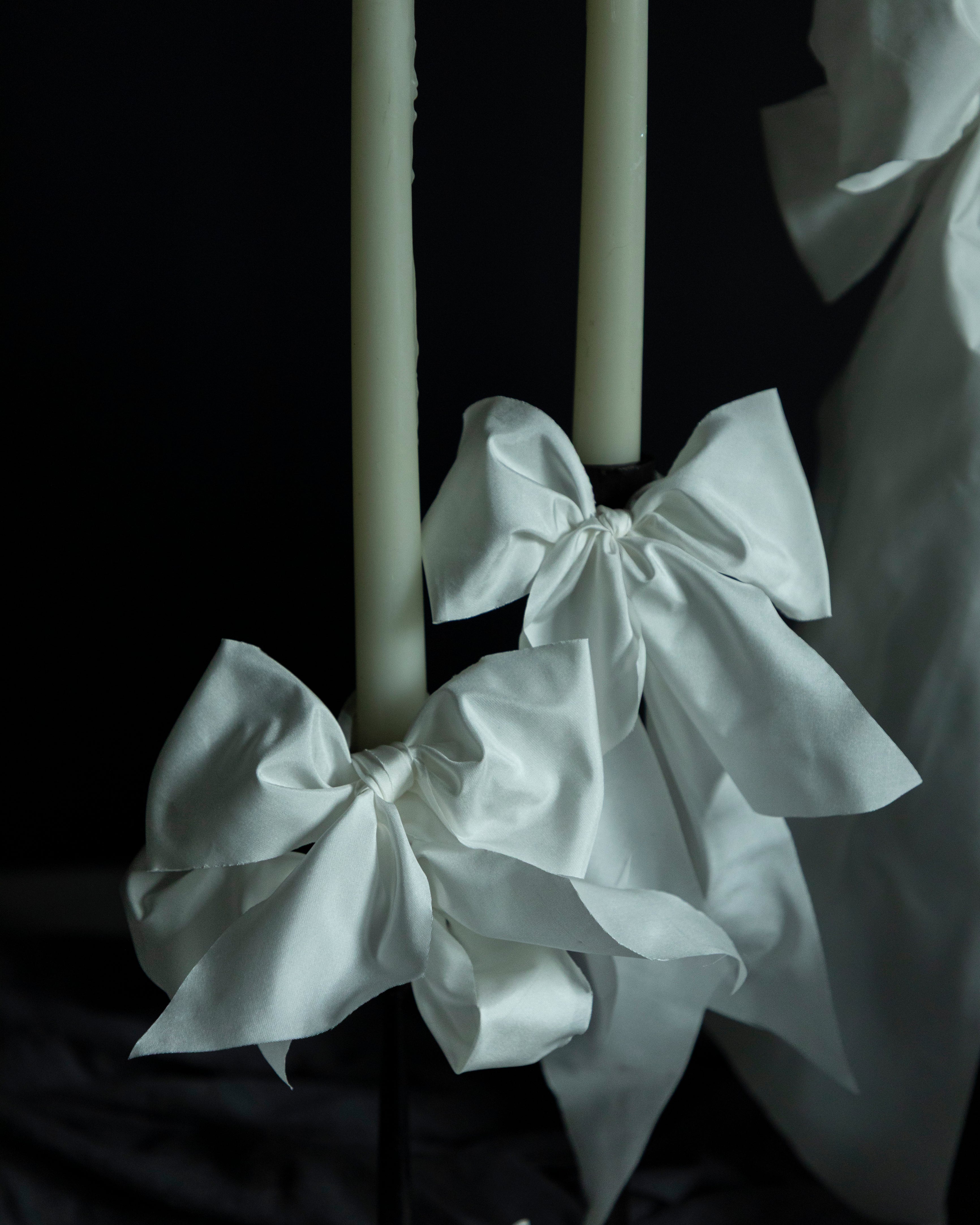 White ribbons tied around a candle against a dark background