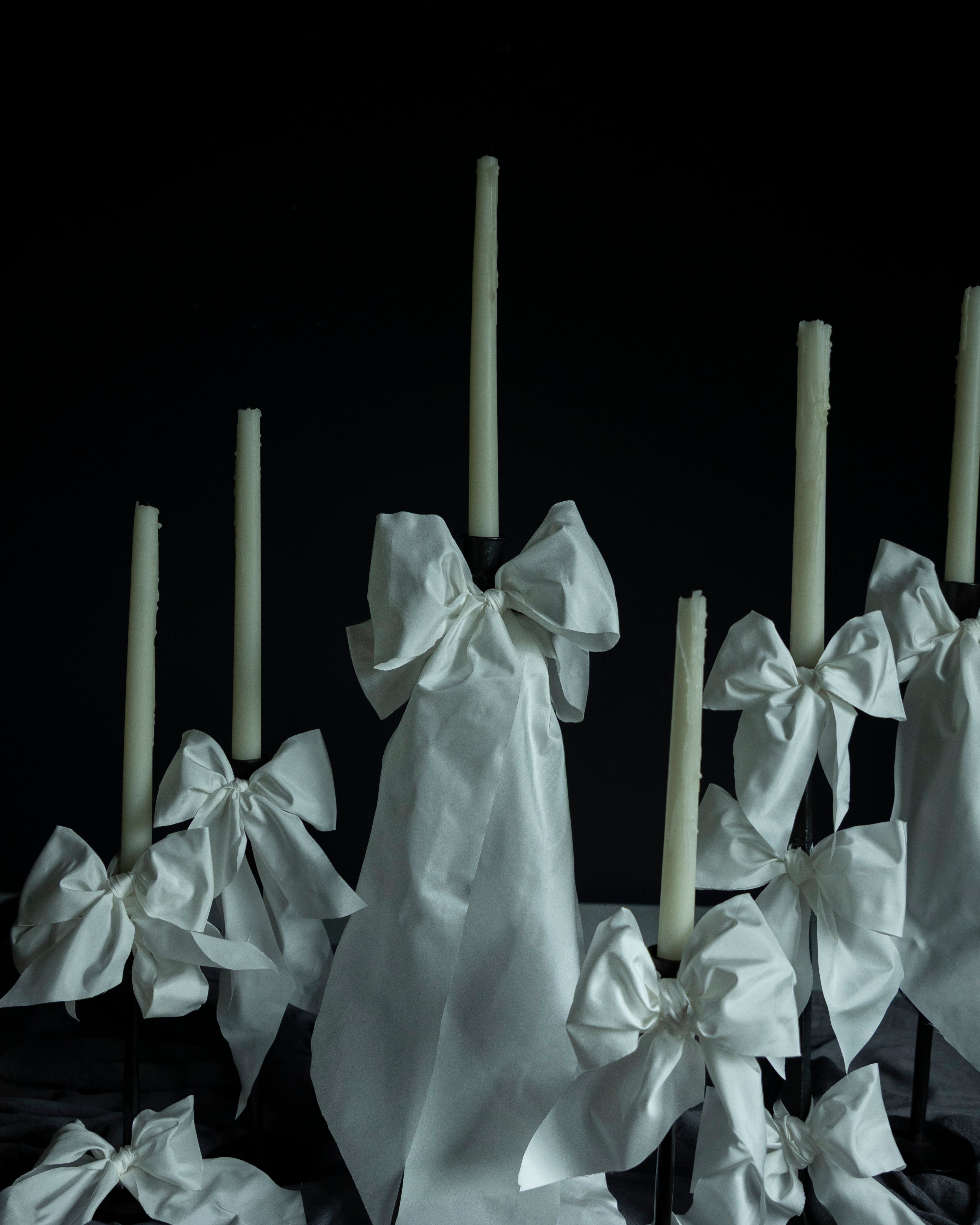 White candles with decorative bows on a dark background