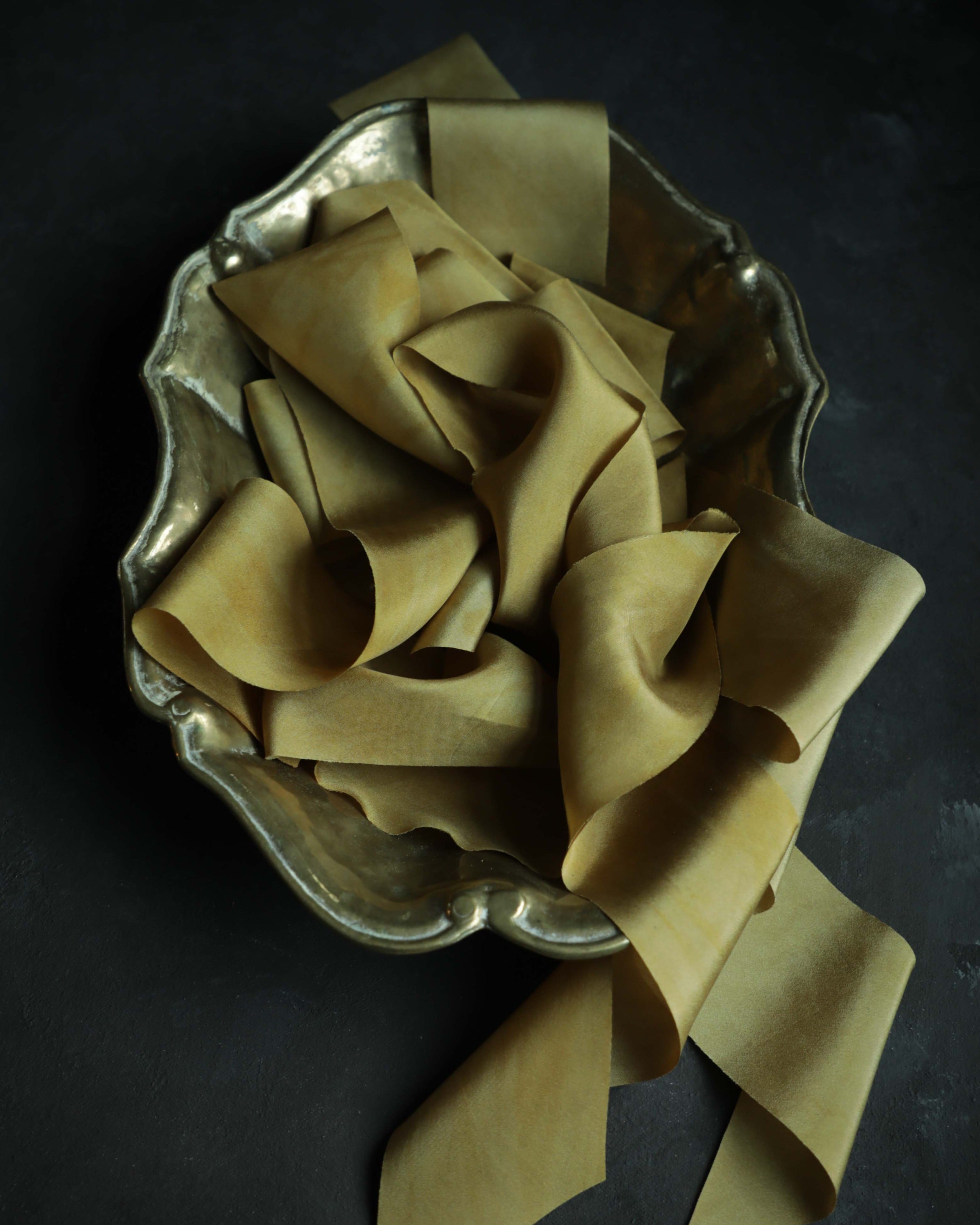 Plant-dyed silk ribbon displayed elegantly in a brass gold bowl, showcasing its luxurious sheen and soft hues, ideal for wrapping bridal bouquets. Perfect for brides-to-be, engaged couples, and florists seeking the world's finest ribbon for wedding flowers.