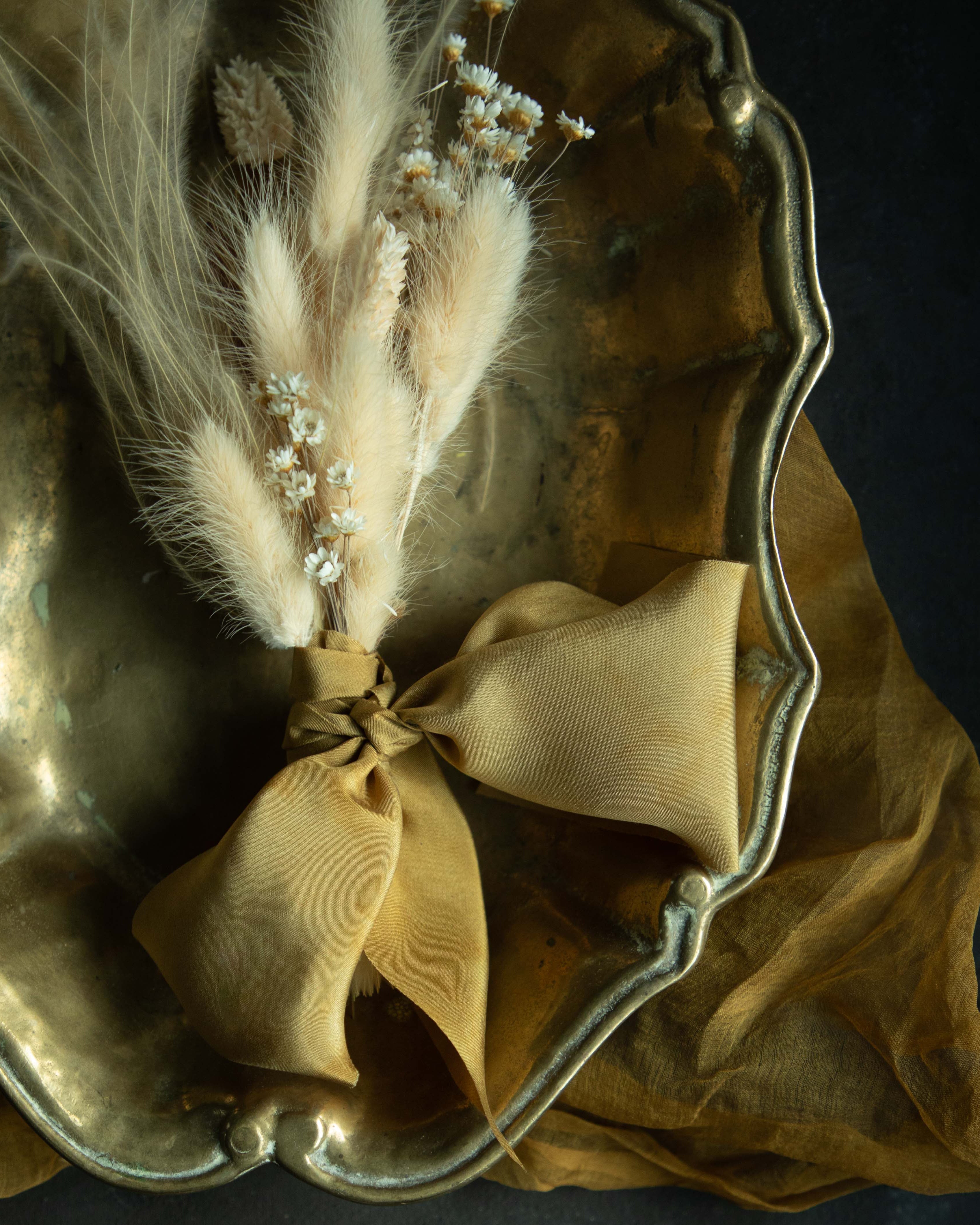 Plant-dyed silk ribbon displayed elegantly in a brass dish, showcasing its luxurious sheen and soft hues, ideal for wrapping bridal bouquets. Perfect for brides-to-be, engaged couples, and florists seeking the world's finest ribbon for wedding flowers.