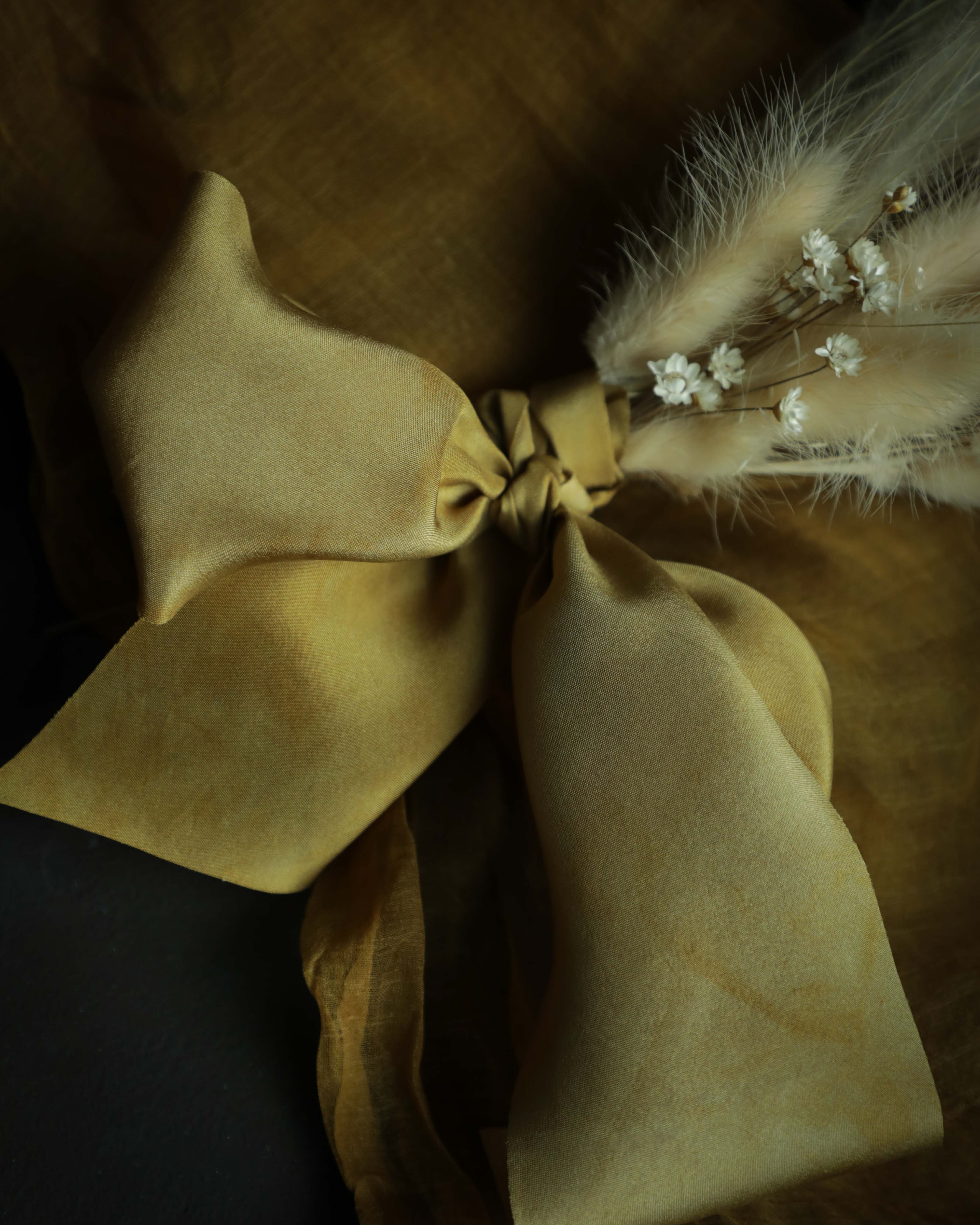 Gold plant-dyed silk ribbon displayed elegantly against a textured background, showcasing its luxurious sheen and soft hues, ideal for wrapping bridal bouquets. Perfect for brides-to-be, engaged couples, and florists seeking the world's finest ribbon for wedding flowers.