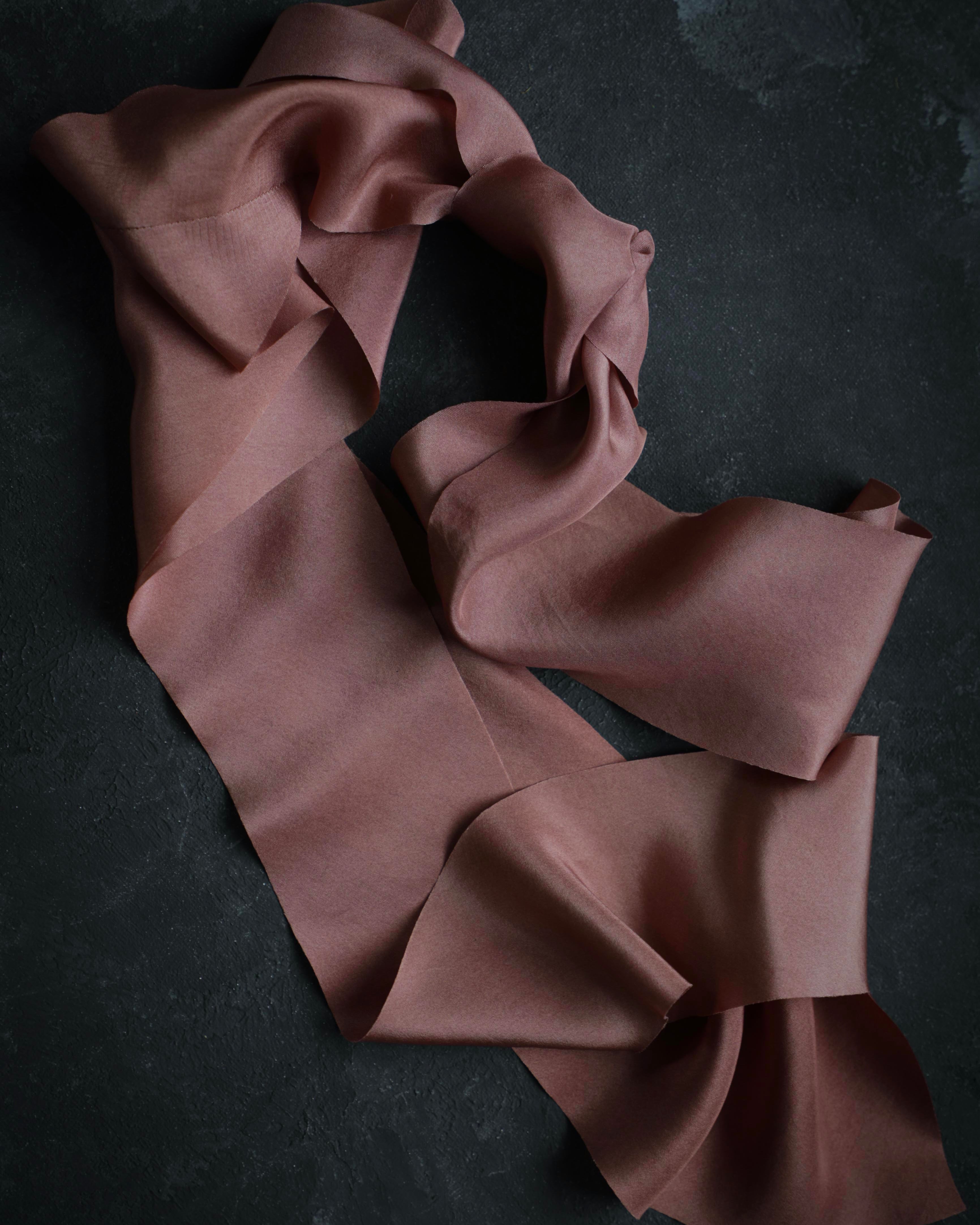 A copper rose colored organic silk ribbon laid out on a dark surface.