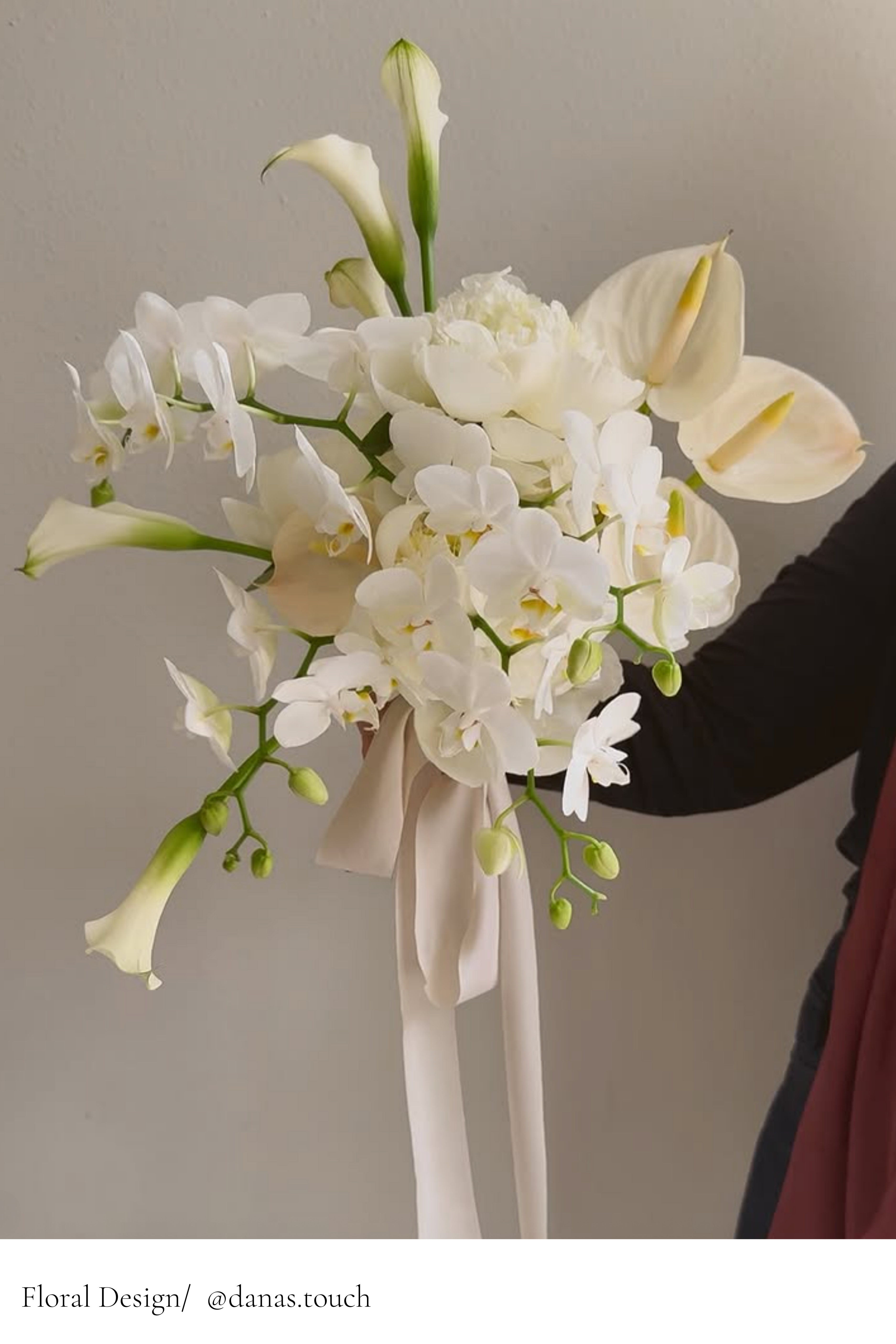 Bouquet of white flowers with a beige ribbon held by a person against a neutral background