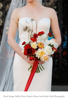 Bride holding a colorful bouquet with red silk ribbon with a blurred background