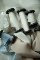 Several spools of satin ribbon in white, beige, and pale blue, arranged on a soft white fabric background.