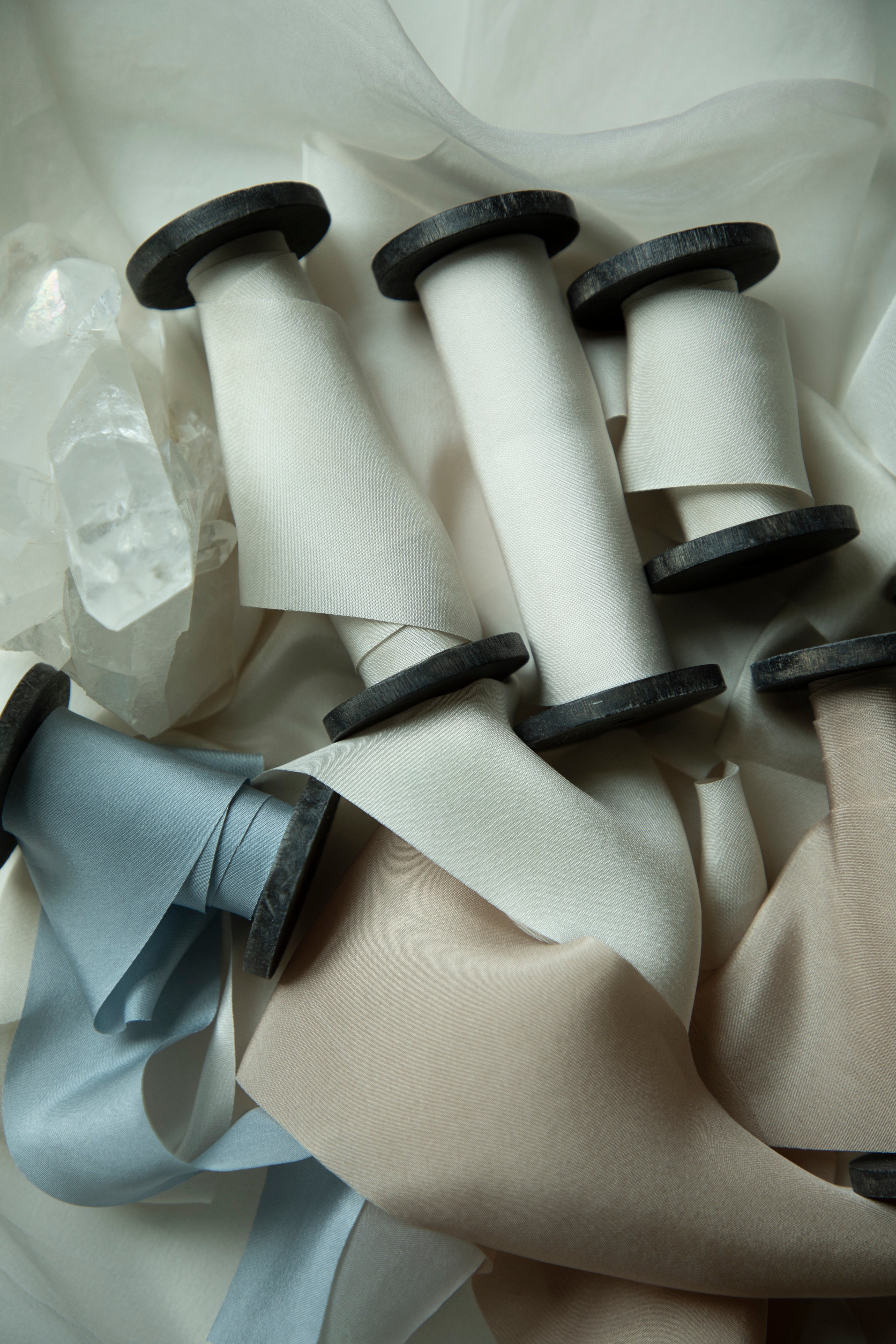 Several spools of satin ribbon in white, beige, and pale blue, arranged on a soft white fabric background.