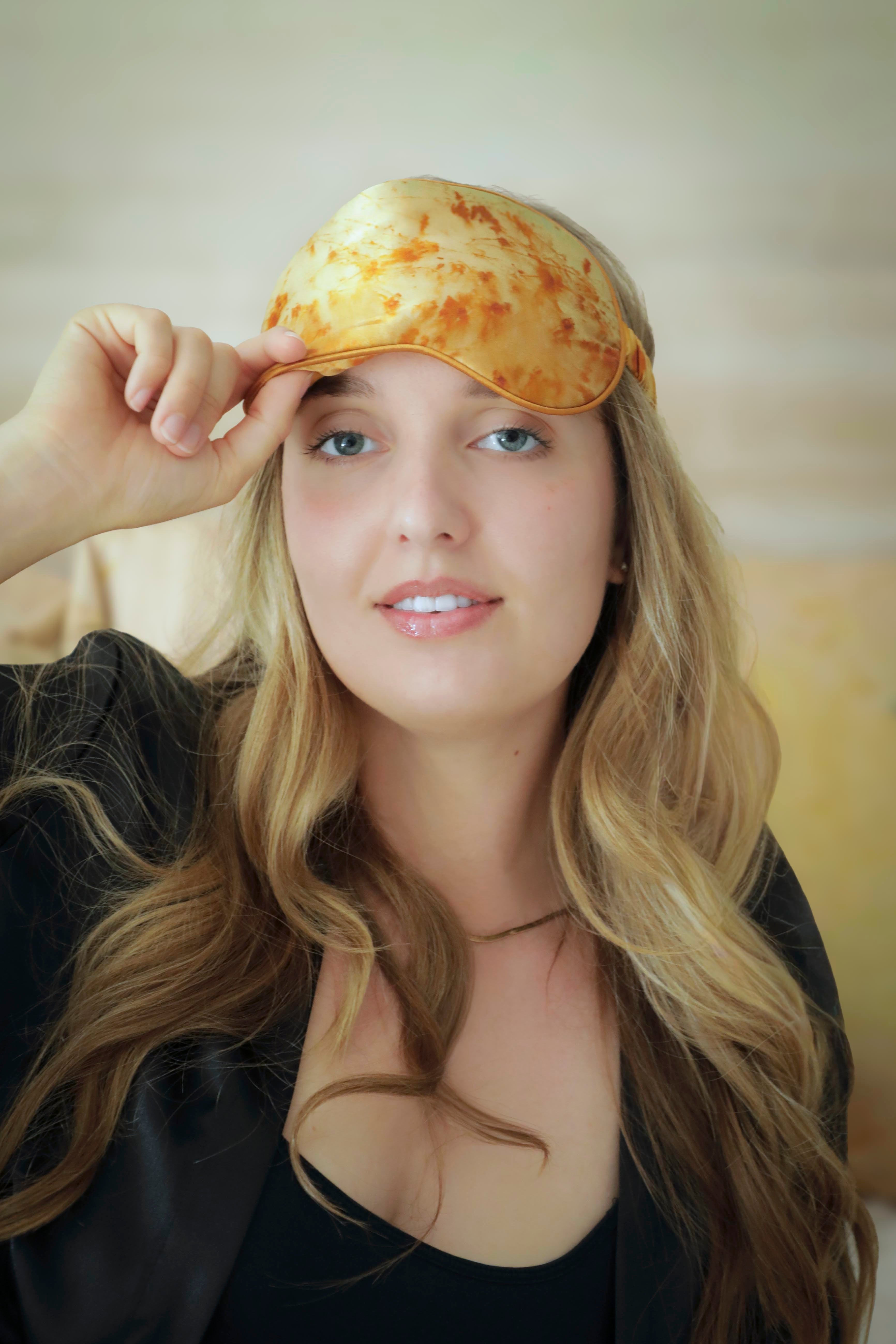 Woman wearing a yellow patterned sleep mask against a neutral background