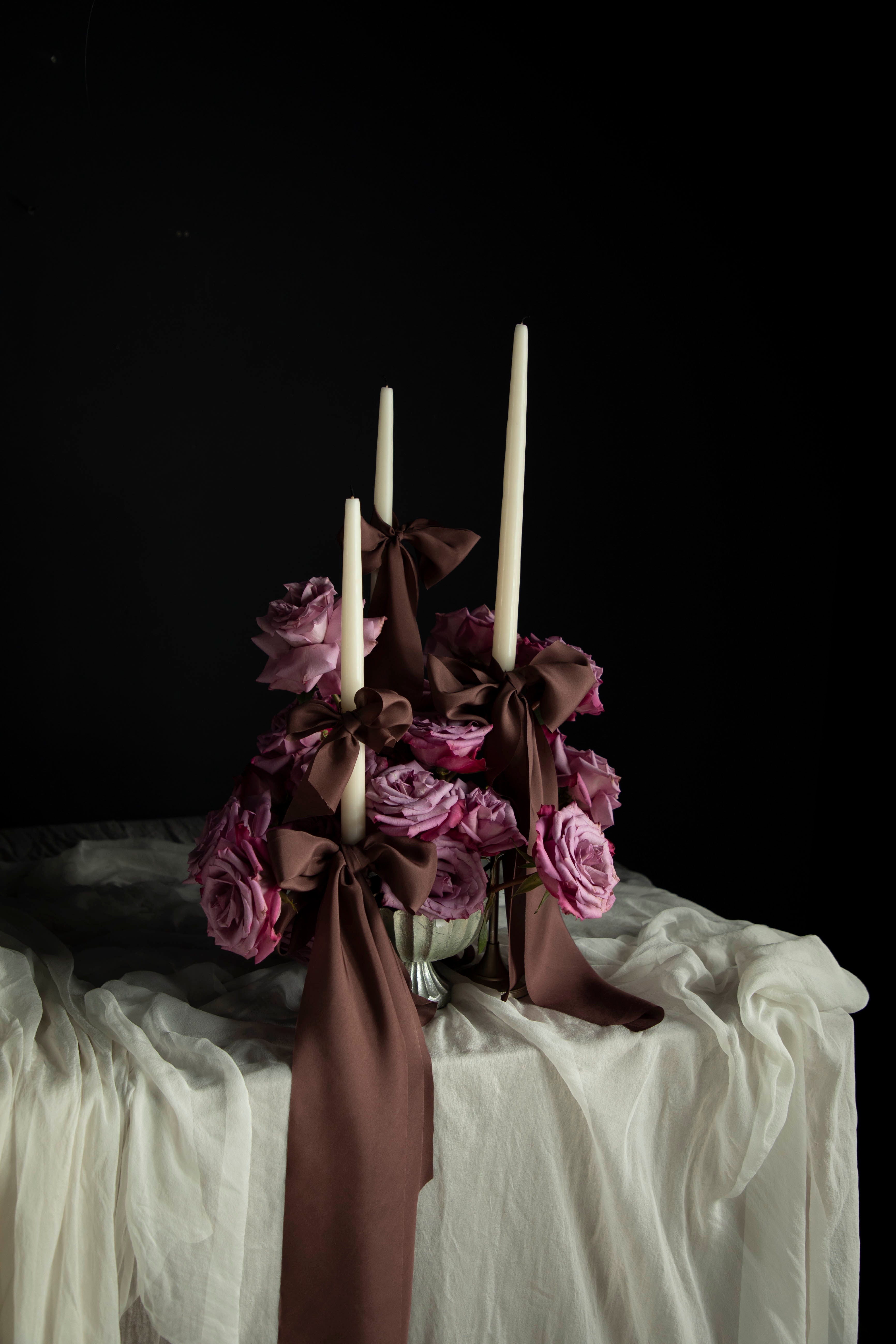 Decorative floral arrangement with candles on a Wedding tablescape with white draping textiles featuring Silk & Willow Chocolate Rose silk ribbons.