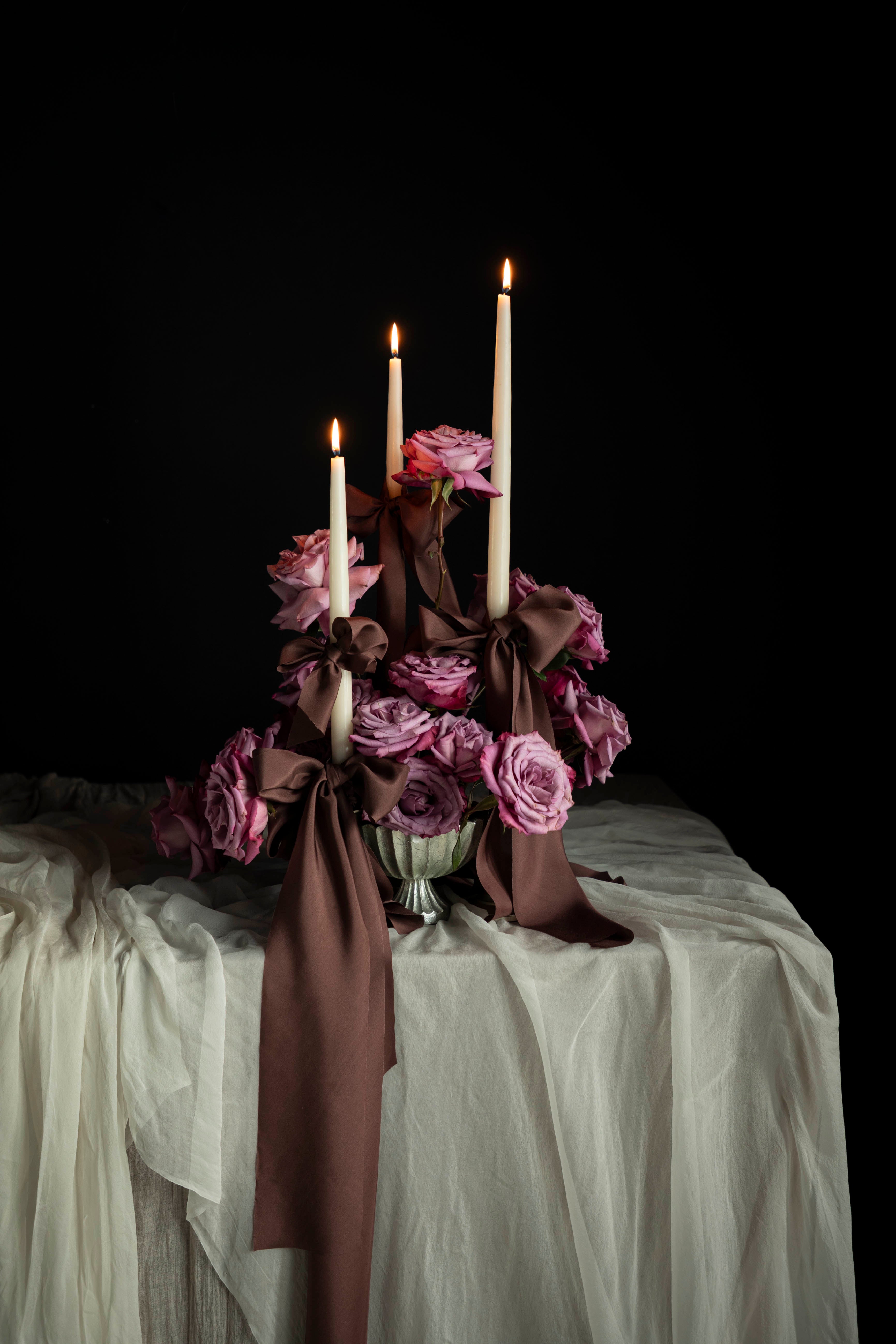 Decorative floral arrangement with candles on a tablecloth against a dark background. Featuring Silk & Willow Chocolate Rose silk ribbons.
