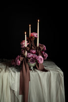 Decorative floral arrangement with candles on a tablecloth against a dark background. Featuring Silk & Willow Chocolate Rose silk ribbons.