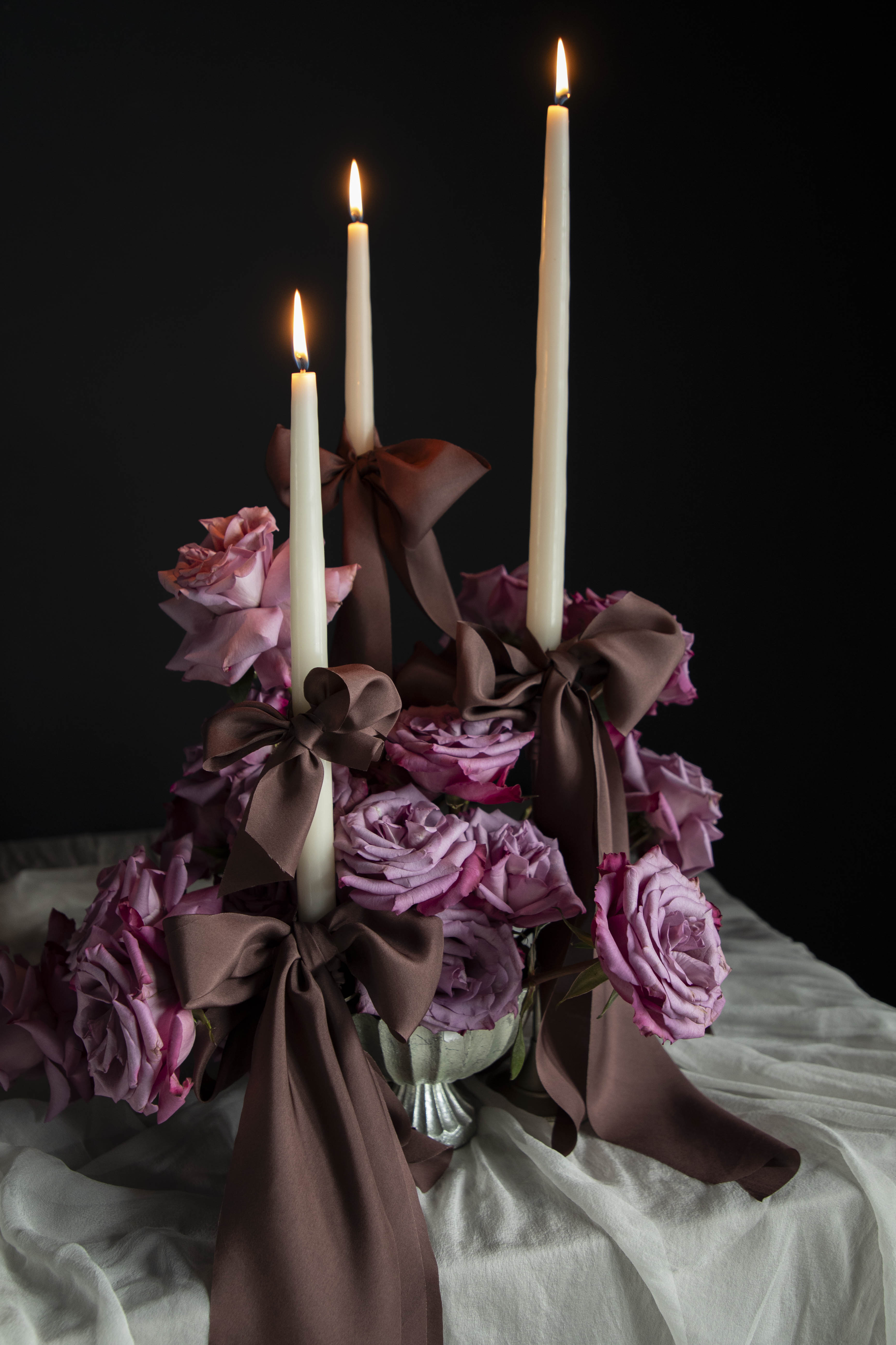 Decorative floral arrangement with candles on a tablecloth against a dark background. Featuring Silk & Willow Chocolate Rose silk ribbons.
