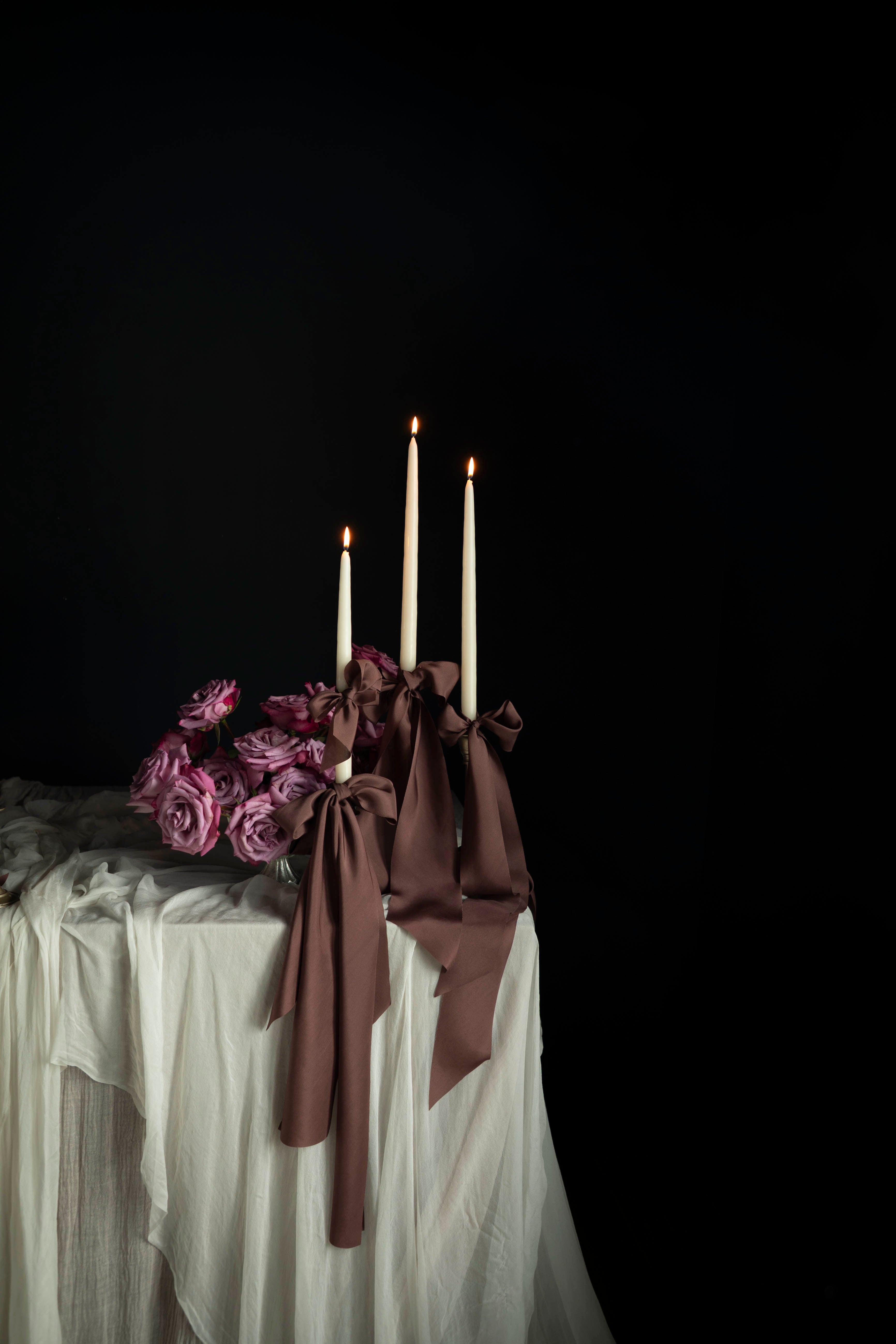 Decorative table setting with candles and flowers against a dark background. Featuring Silk & Willow Chocolate Rose silk ribbons.