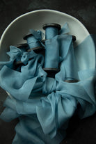 Duchess Blue silk ribbon wrapped around wooden spools inside a white bowl on a dark surface