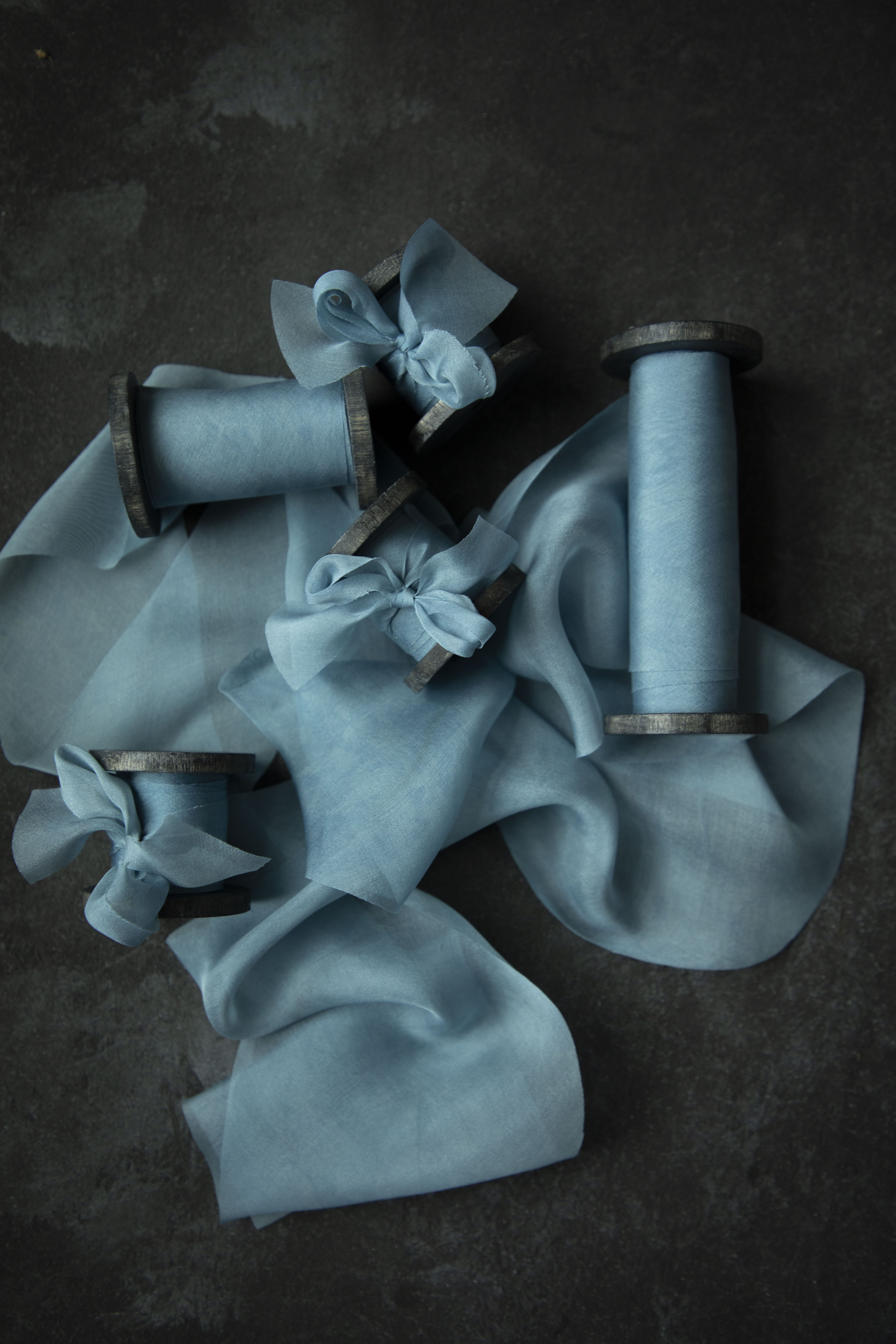 Duchess Blue silk ribbon with wooden spools on a dark background