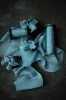 Duchess Blue silk ribbon with wooden spools on a dark background