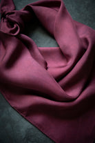 A draped mauve-purple scarf with a satin-like sheen, styled in soft folds on a dark textured background.