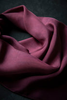 A draped piece of deep burgundy silk fabric with soft folds and a subtle sheen, set against a dark textured background.