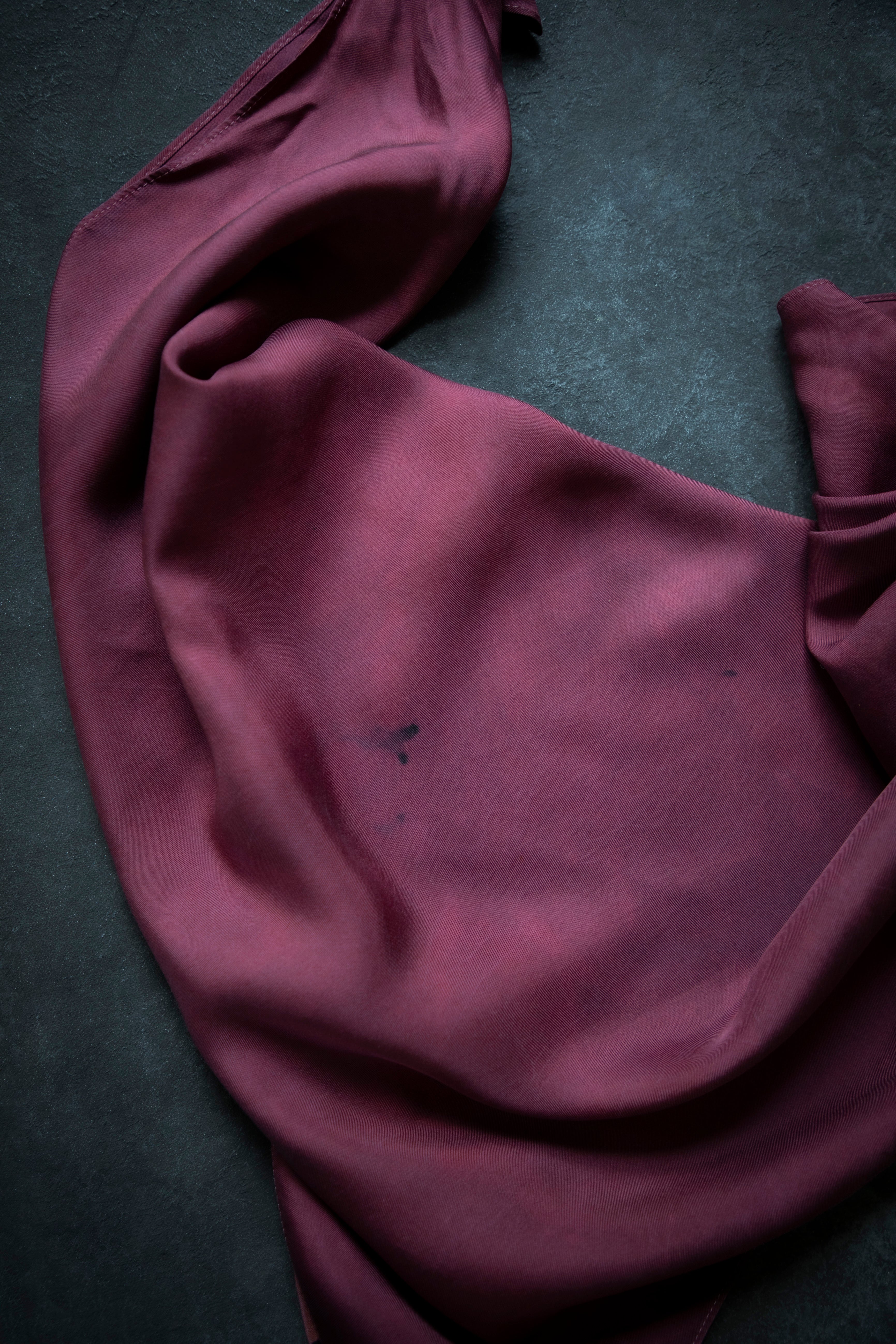 A draped piece of deep plum purple fabric, likely silk or satin, laid out on a dark textured gray surface.