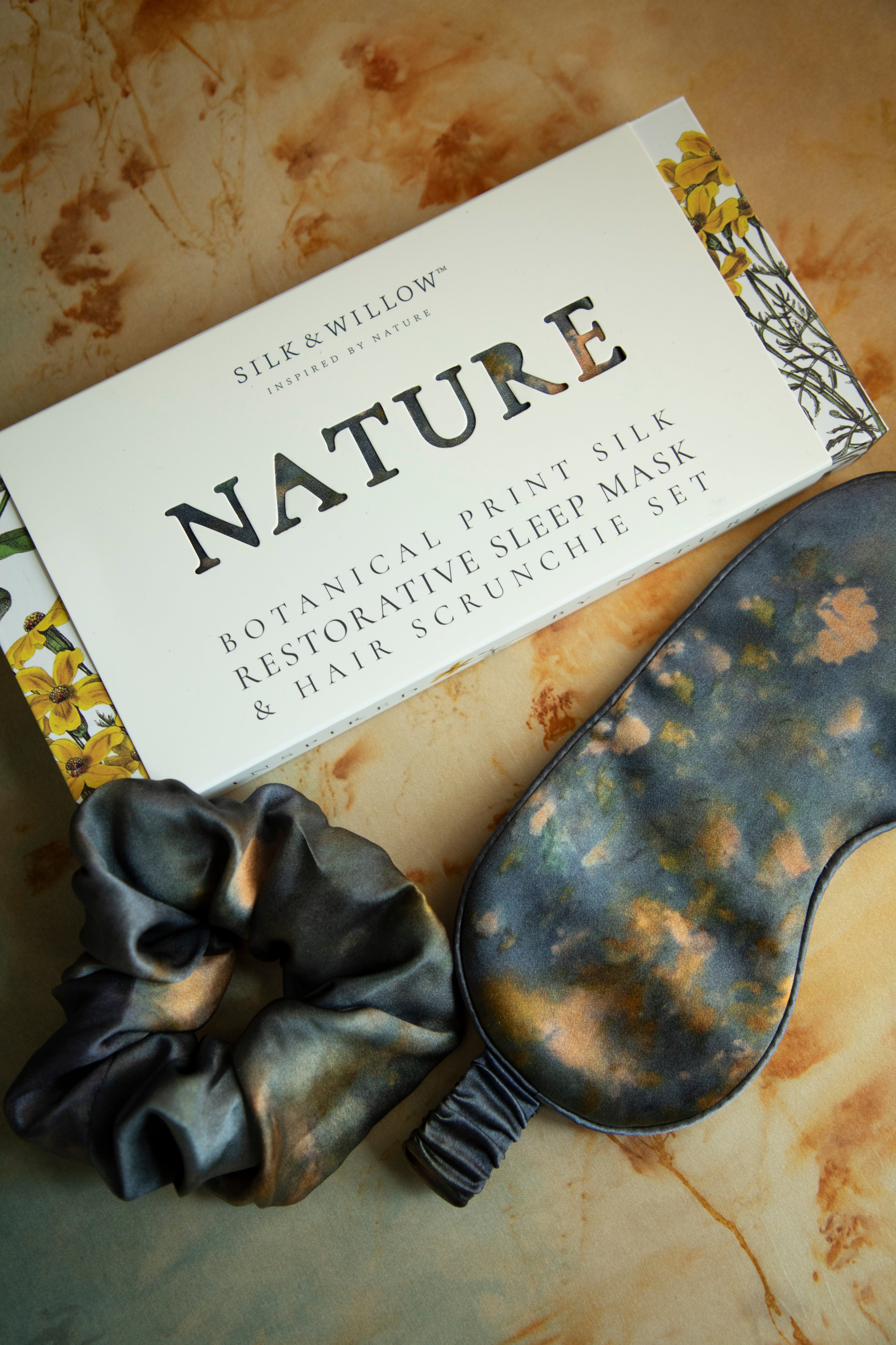 A luxurious silk sleep mask and hair scrunchie set featuring delicate botanical patterns, elegantly displayed in a sustainable gift box, perfect for a sophisticated and eco-conscious touch.