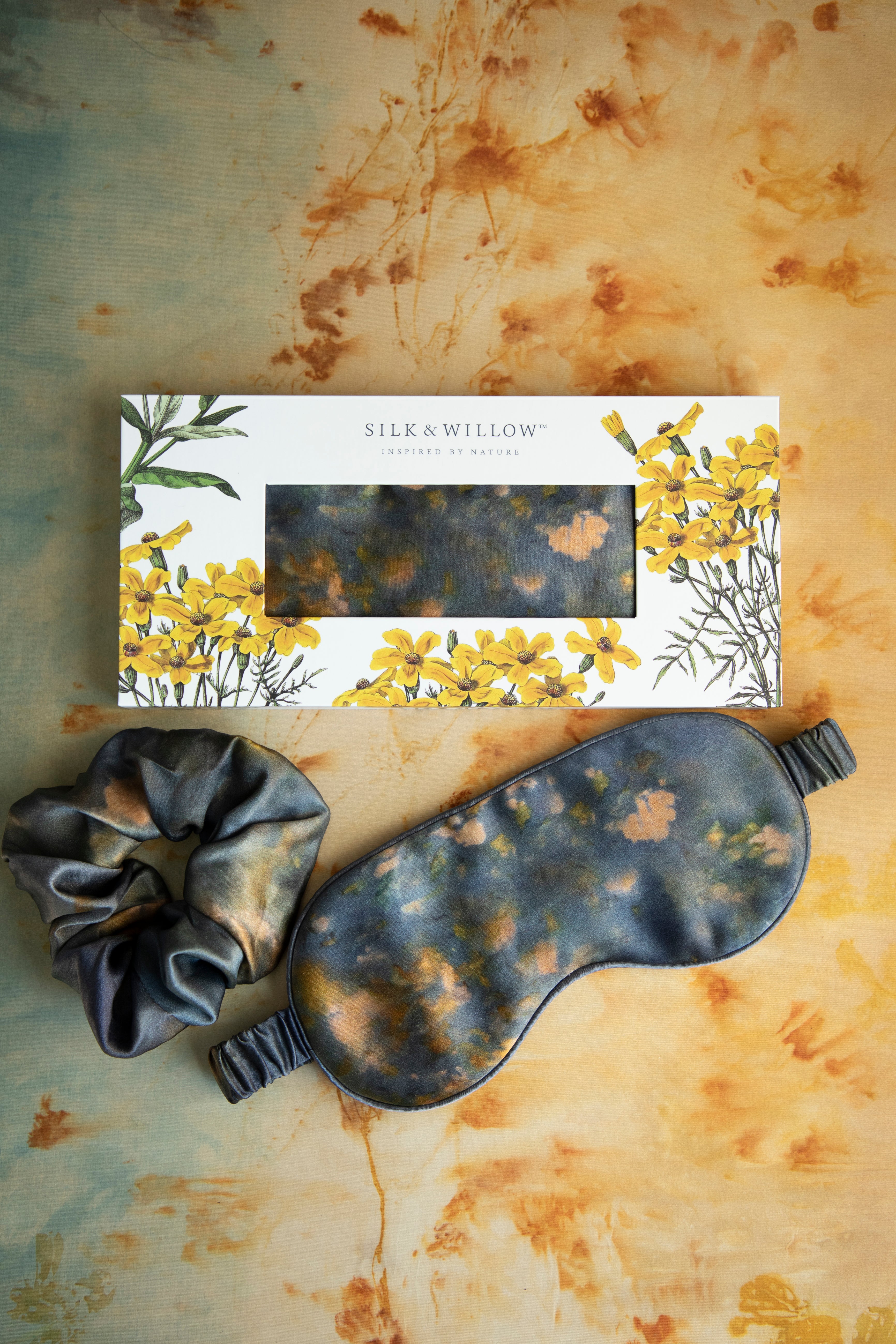A luxurious silk sleep mask and hair scrunchie set featuring delicate botanical patterns, elegantly displayed in a sustainable gift box, perfect for a sophisticated and eco-conscious touch.