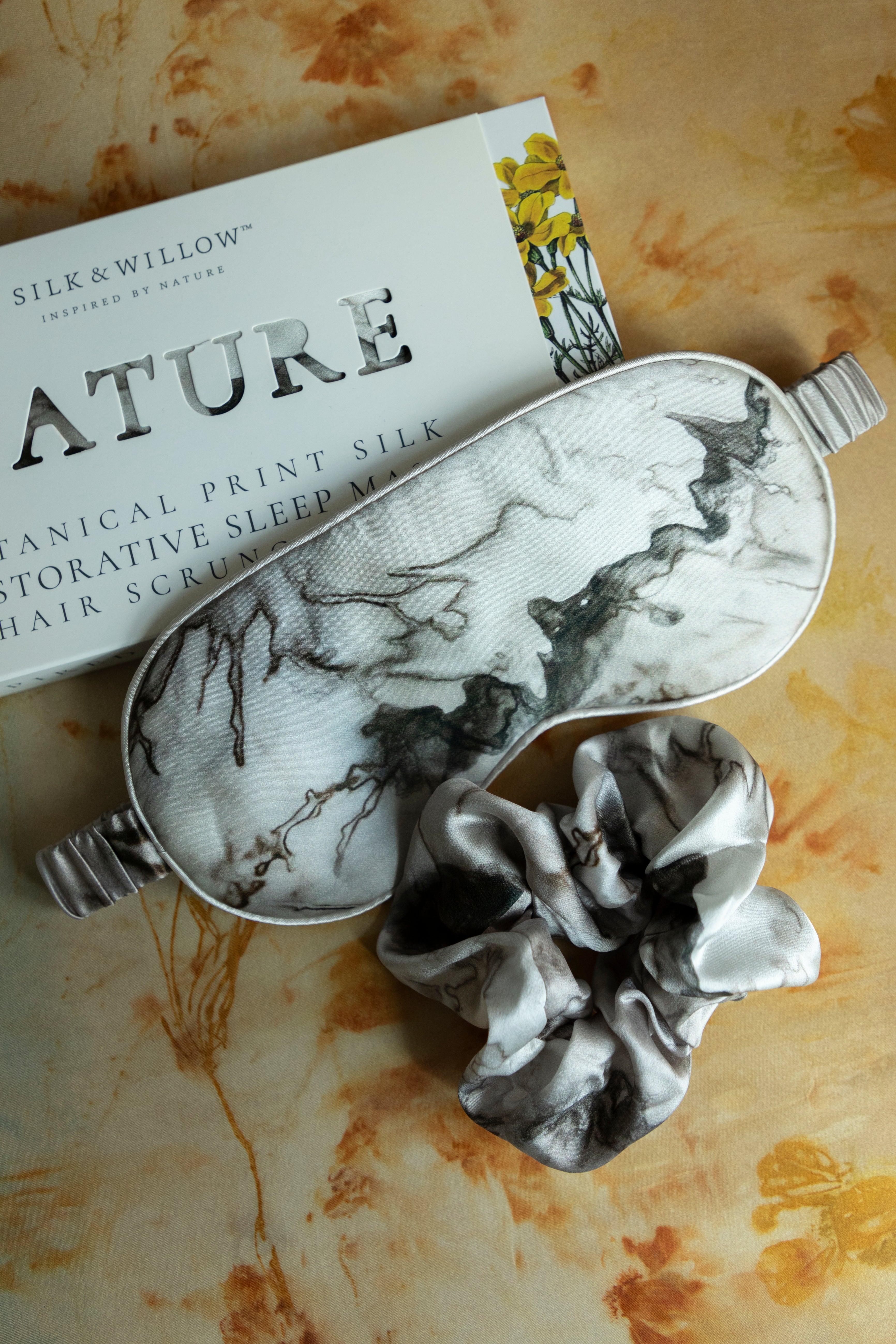 A luxurious silk sleep mask and hair scrunchie set featuring delicate botanical patterns, elegantly displayed in a sustainable gift box, perfect for a sophisticated and eco-conscious touch.