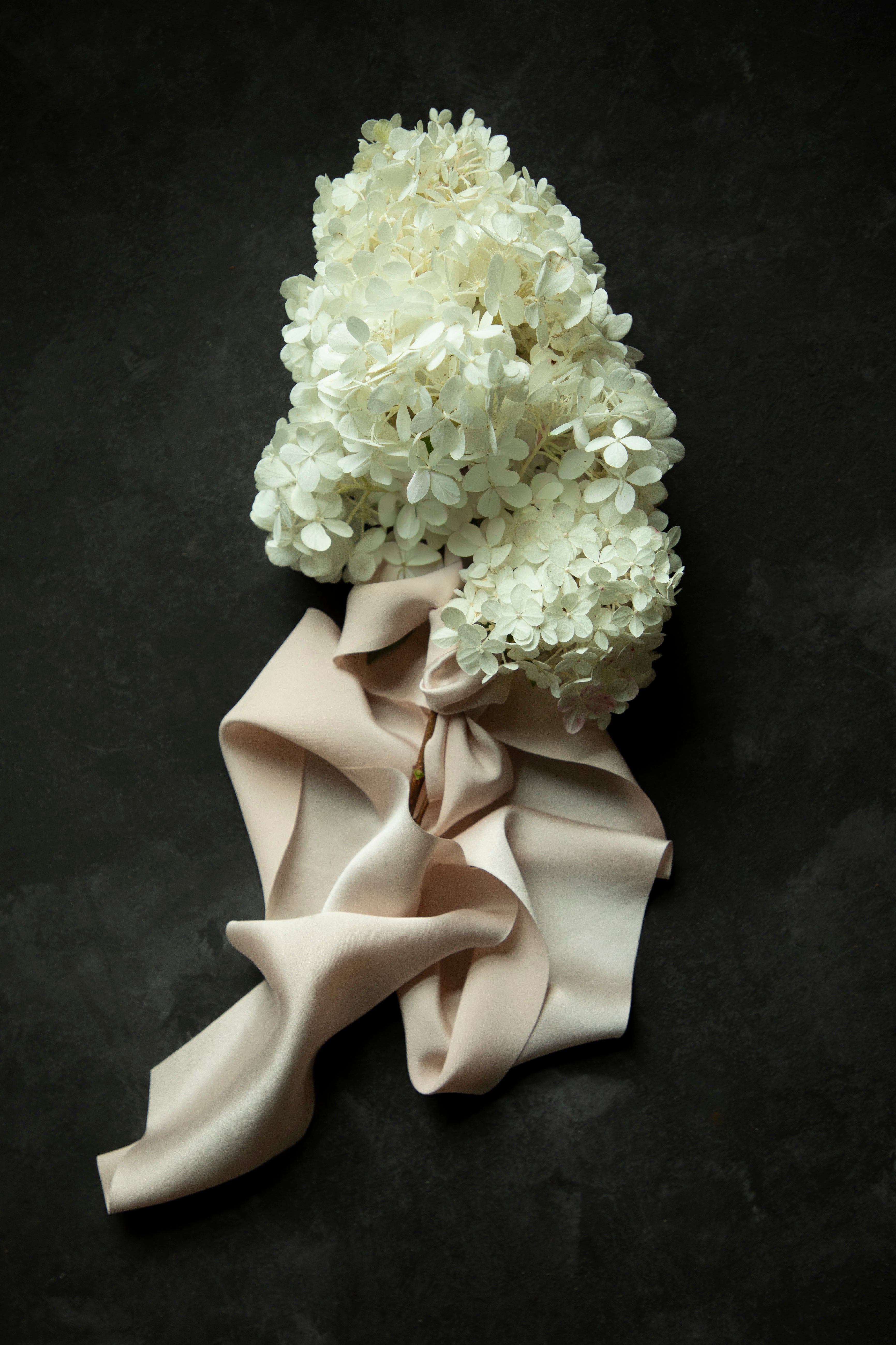 White hydrangea flower bouquet wrapped with a premium bridal silk satin ribbon, laid flat on a dark textured background.