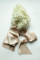 White hydrangea bouquet with a large blush satin ribbon bow, laid flat on a light background.