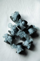 A group of small black wood spools wrapped with sheer pale blue ribbon bows, arranged on a light gray textured background.
